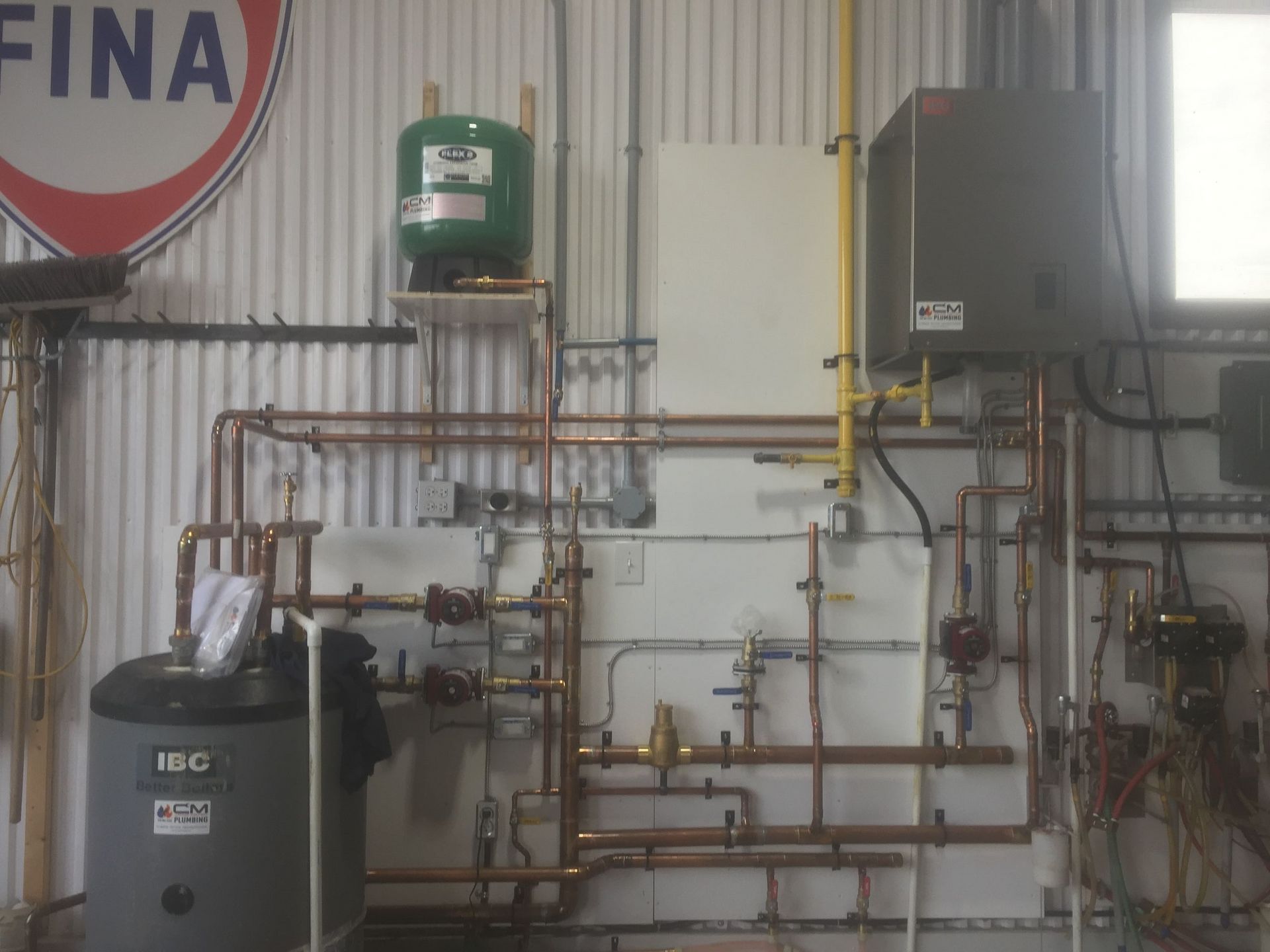 Complex copper pipe heating system with tanks and valves on a white wall.