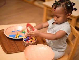 Child sorting colorful objects with tweezers in a Montessori activity that builds focus and fine mot