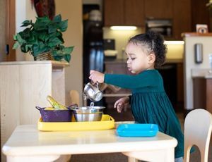 Toddler pouring water in a Montessori Practical Life activity, practicing independence and coordinat