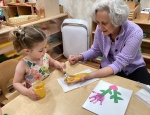 A child and an adult painting with handprints inside a Montessori classroom.