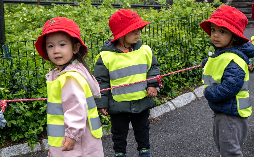 Three children in red hats and safety vests stand outside.
