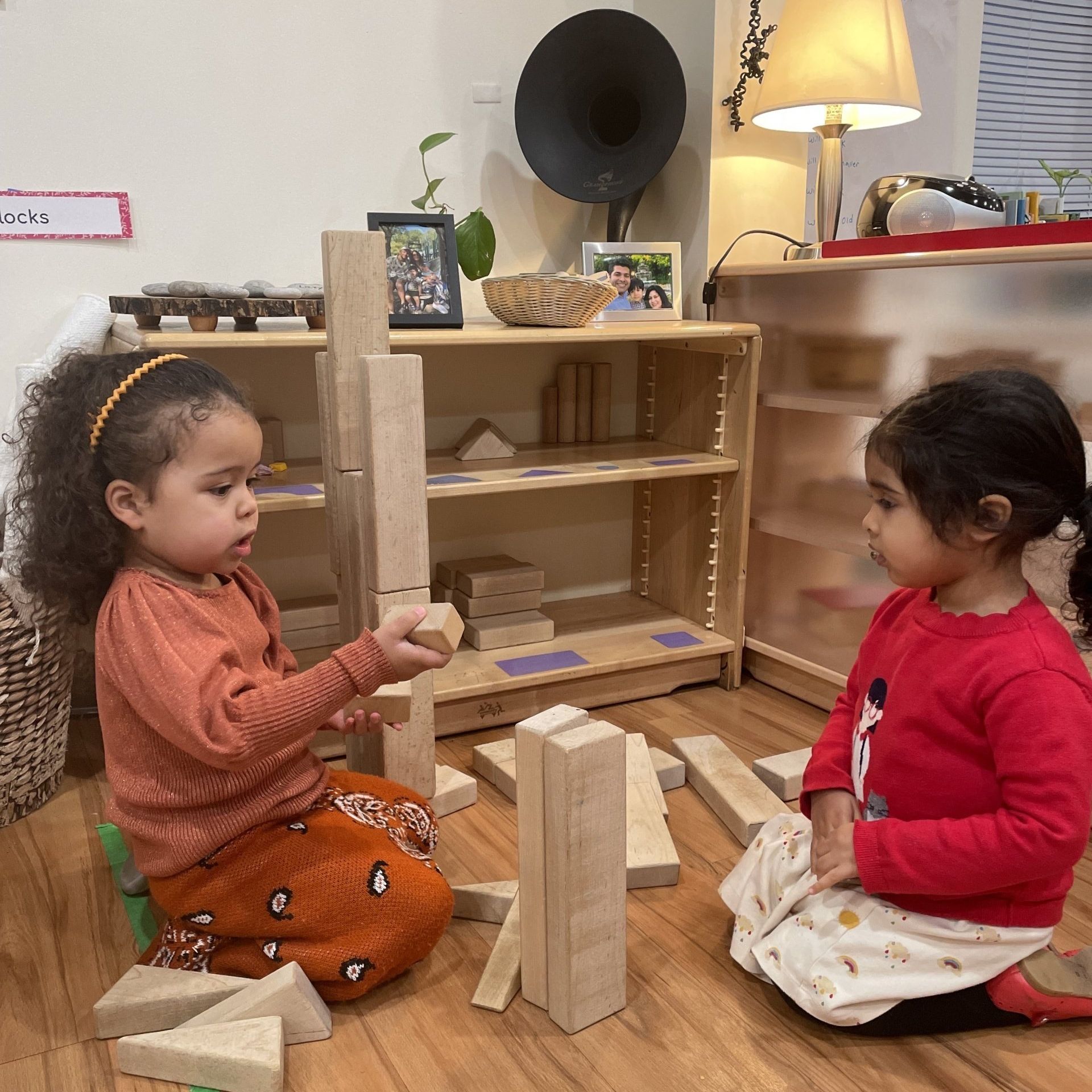 Two young children build with wooden blocks on the floor.