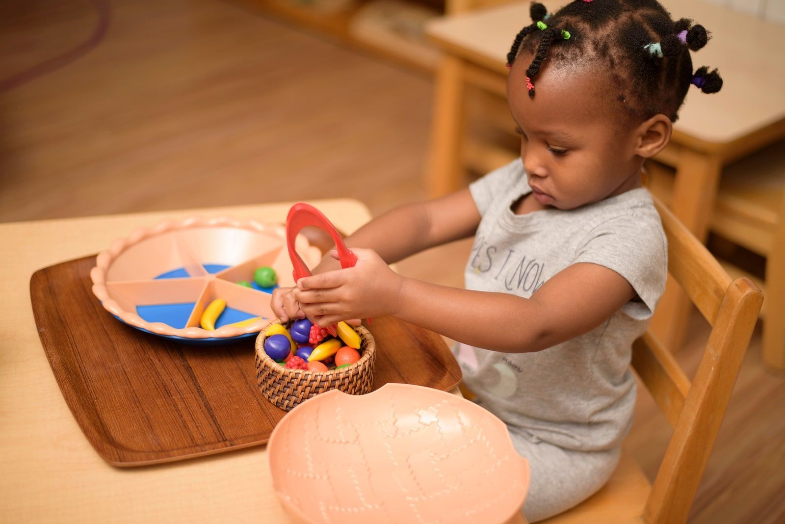 Child sorting colorful objects with tweezers in a Montessori activity that builds focus and fine motor skills.
