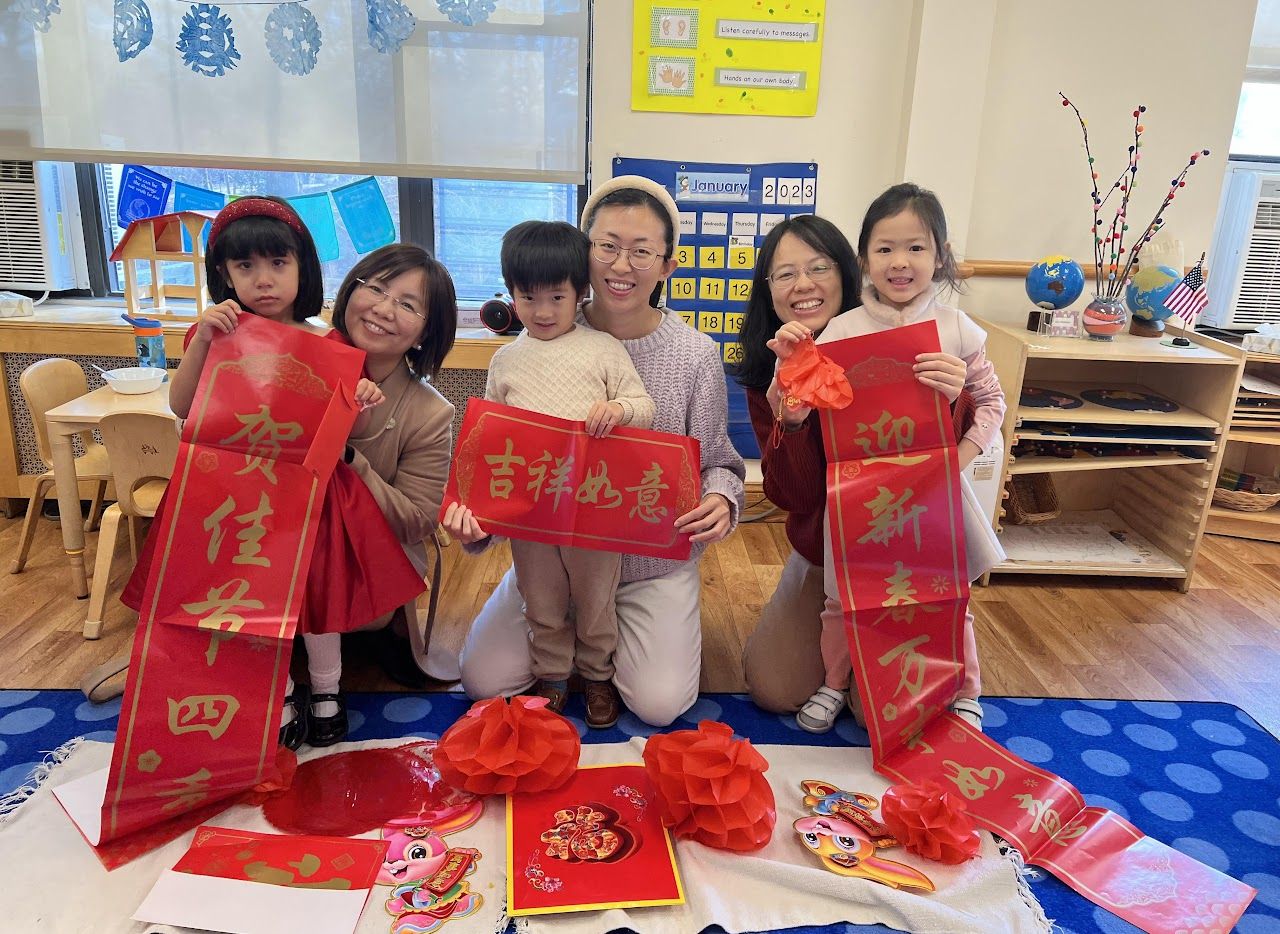 Group of people and children with red Chinese New Year decorations in a classroom setting.