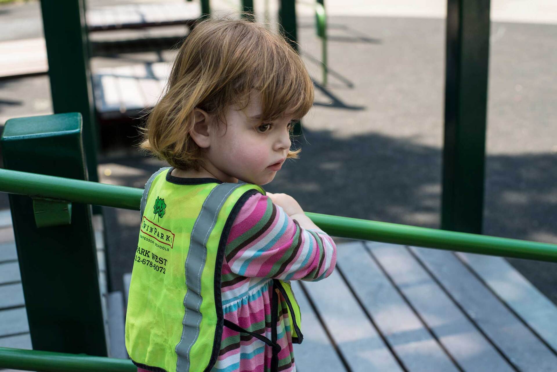 Montessori child wearing a neon vest, looking to the side on a playground.