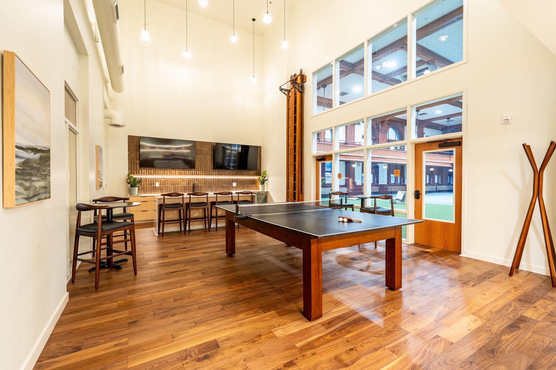 Spacious recreation room with pool table, bar, TVs, and large windows looking outside.