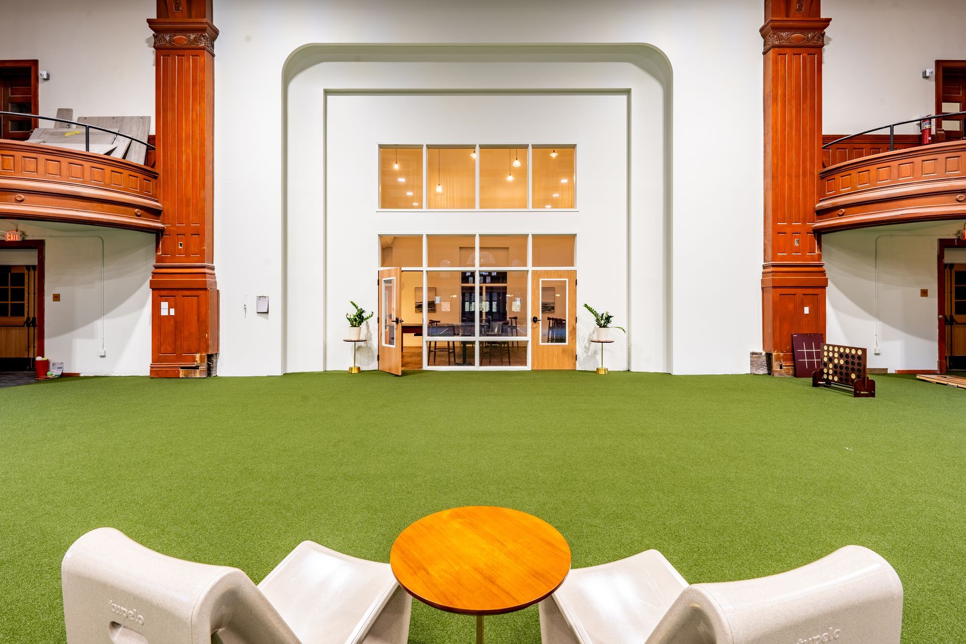 Indoor space with artificial turf, white chairs, wooden table, and a large glass door.