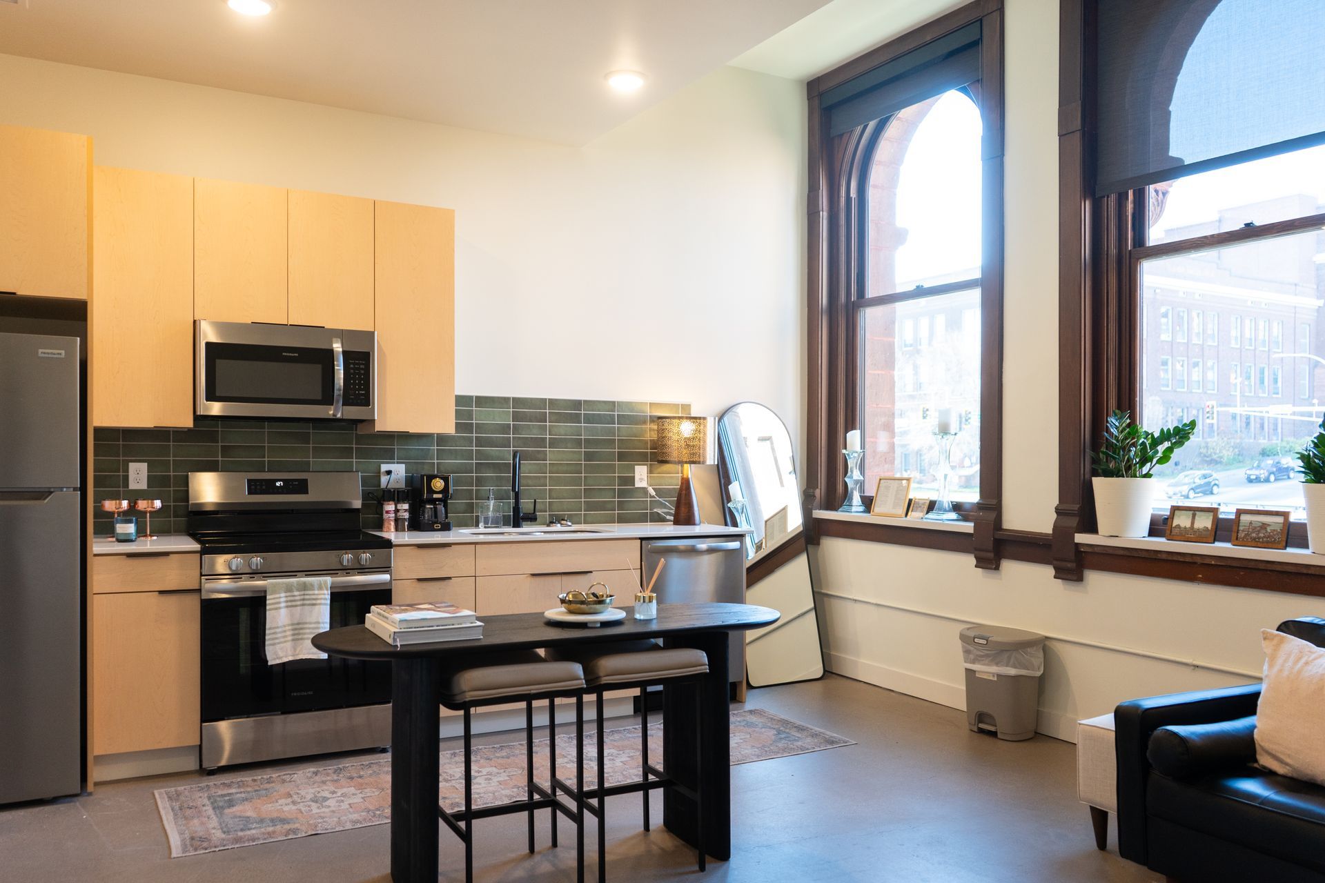 Modern kitchen with stainless steel appliances, light wood cabinets, and a black table with stools.