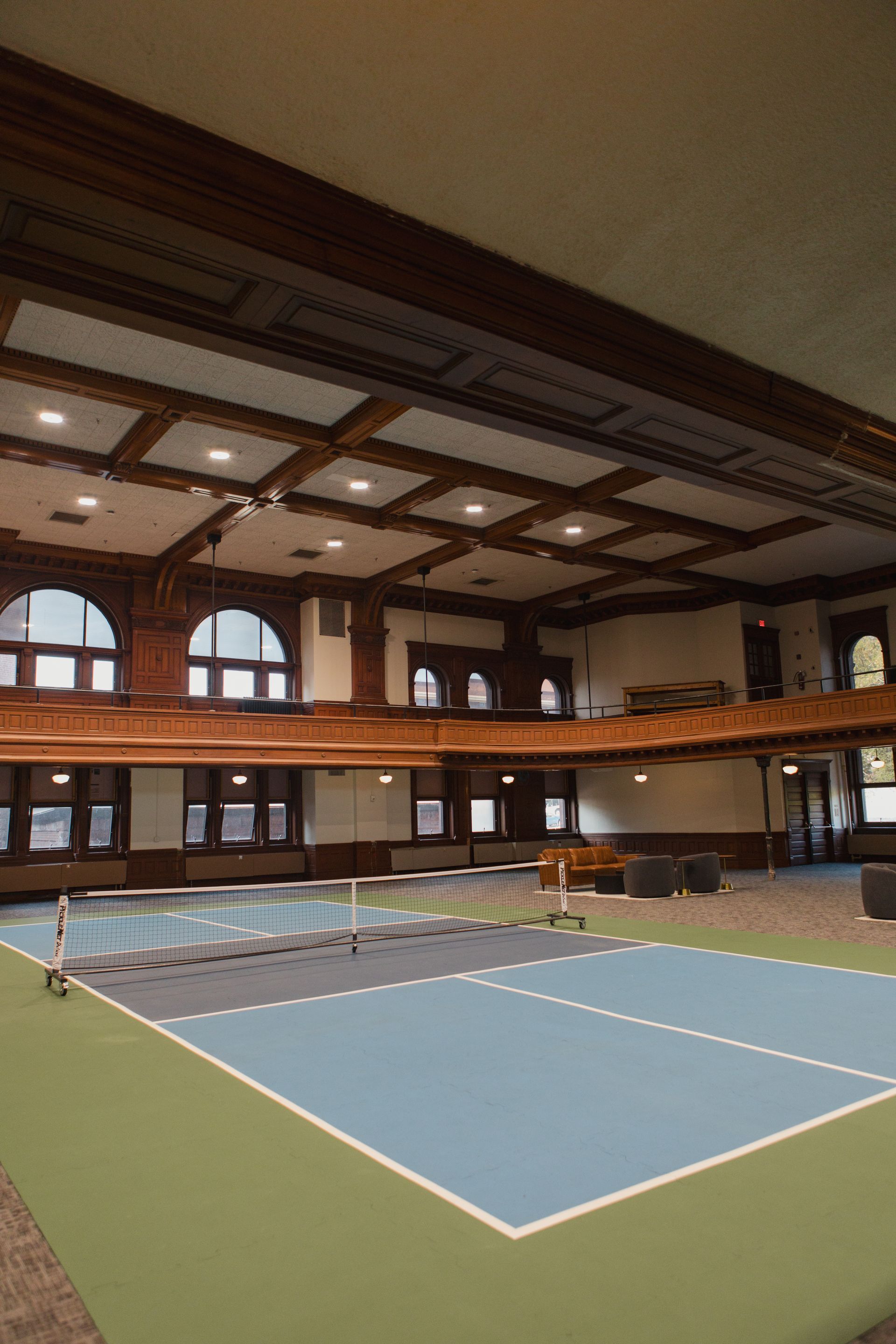 Indoor tennis court with blue and green court, dark wood trim, and a balcony.