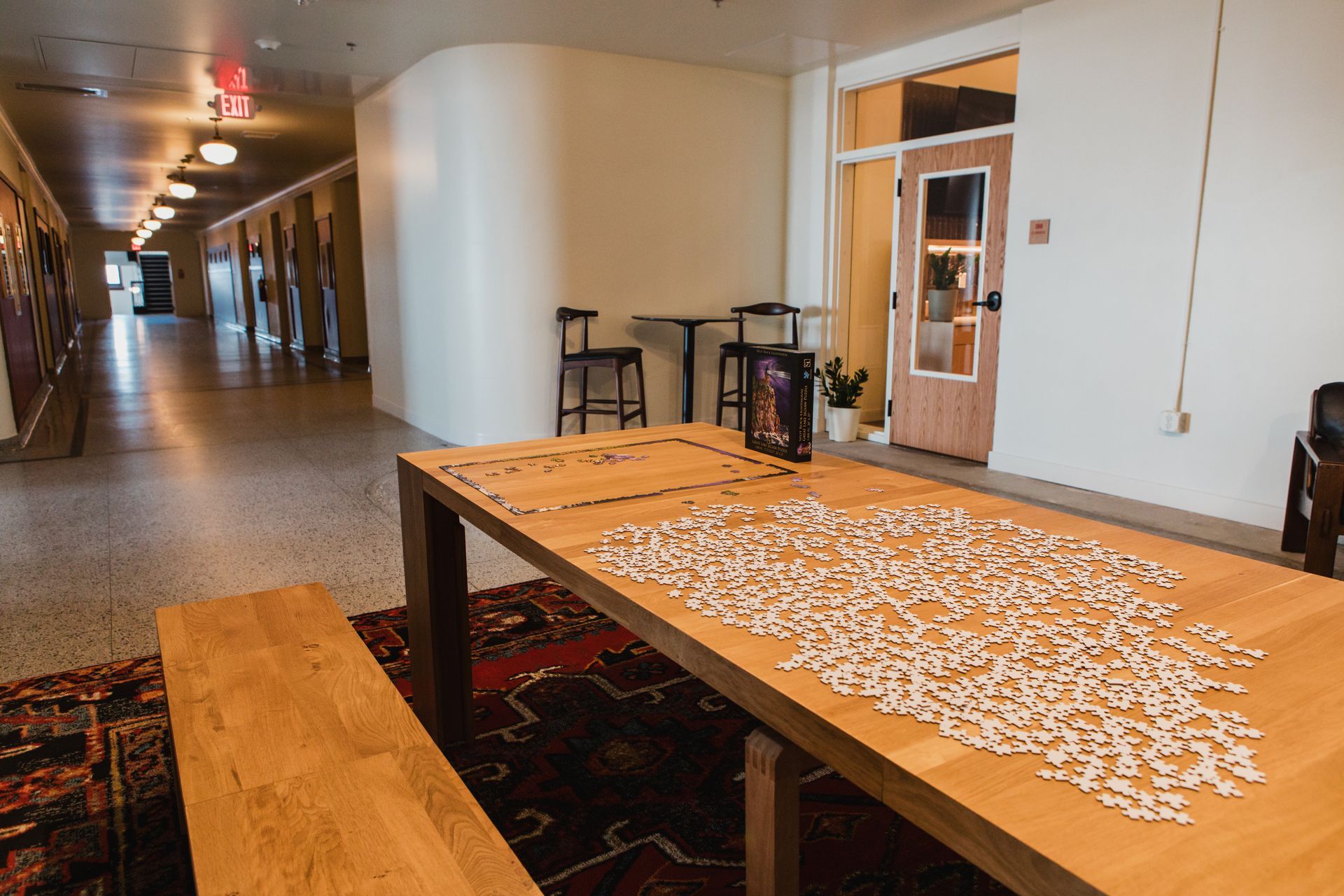 Long hallway with wood table covered in puzzle pieces, bench, rug, and arched wall.