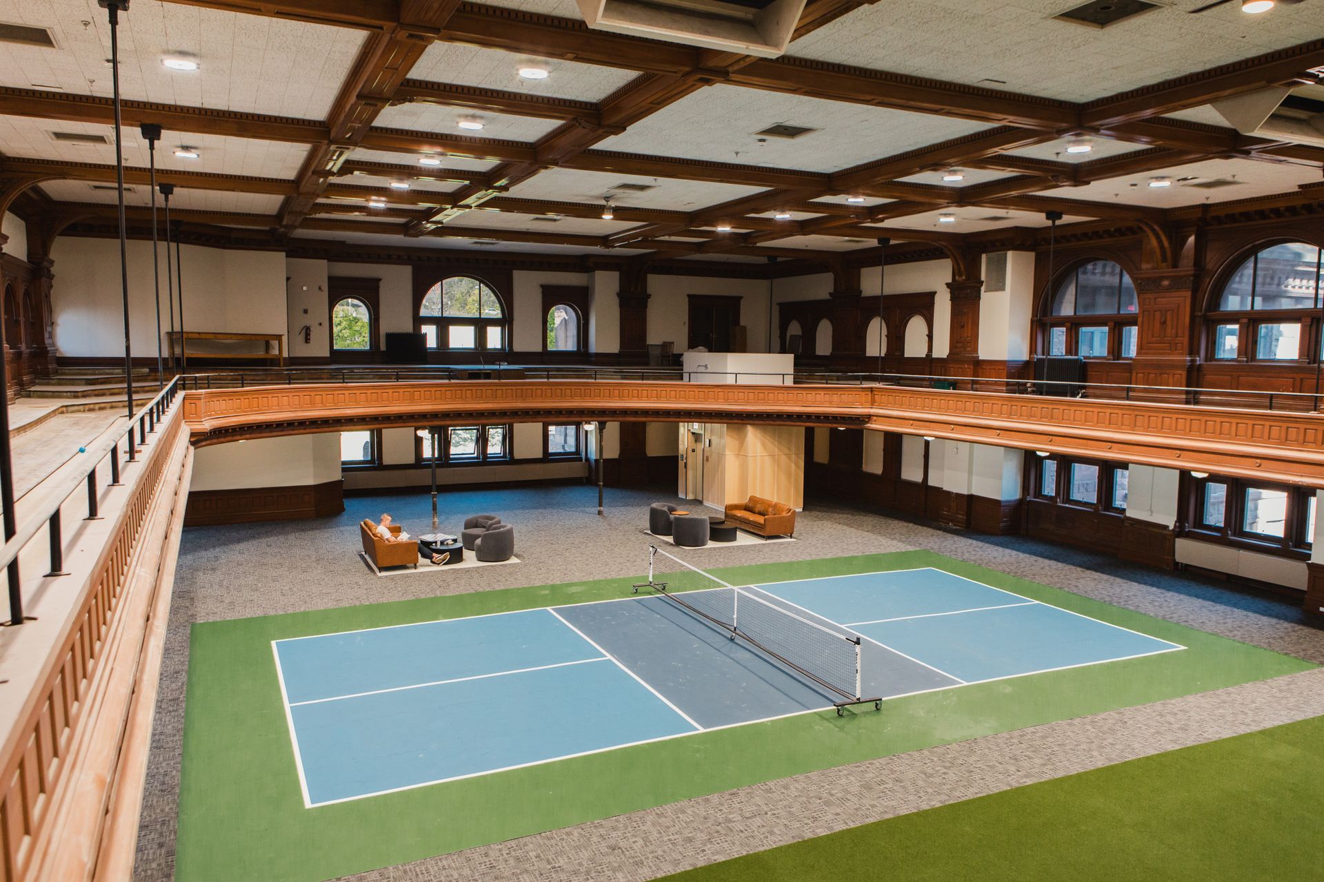 Indoor pickleball court with blue and green flooring, surrounded by a wood-paneled balcony.