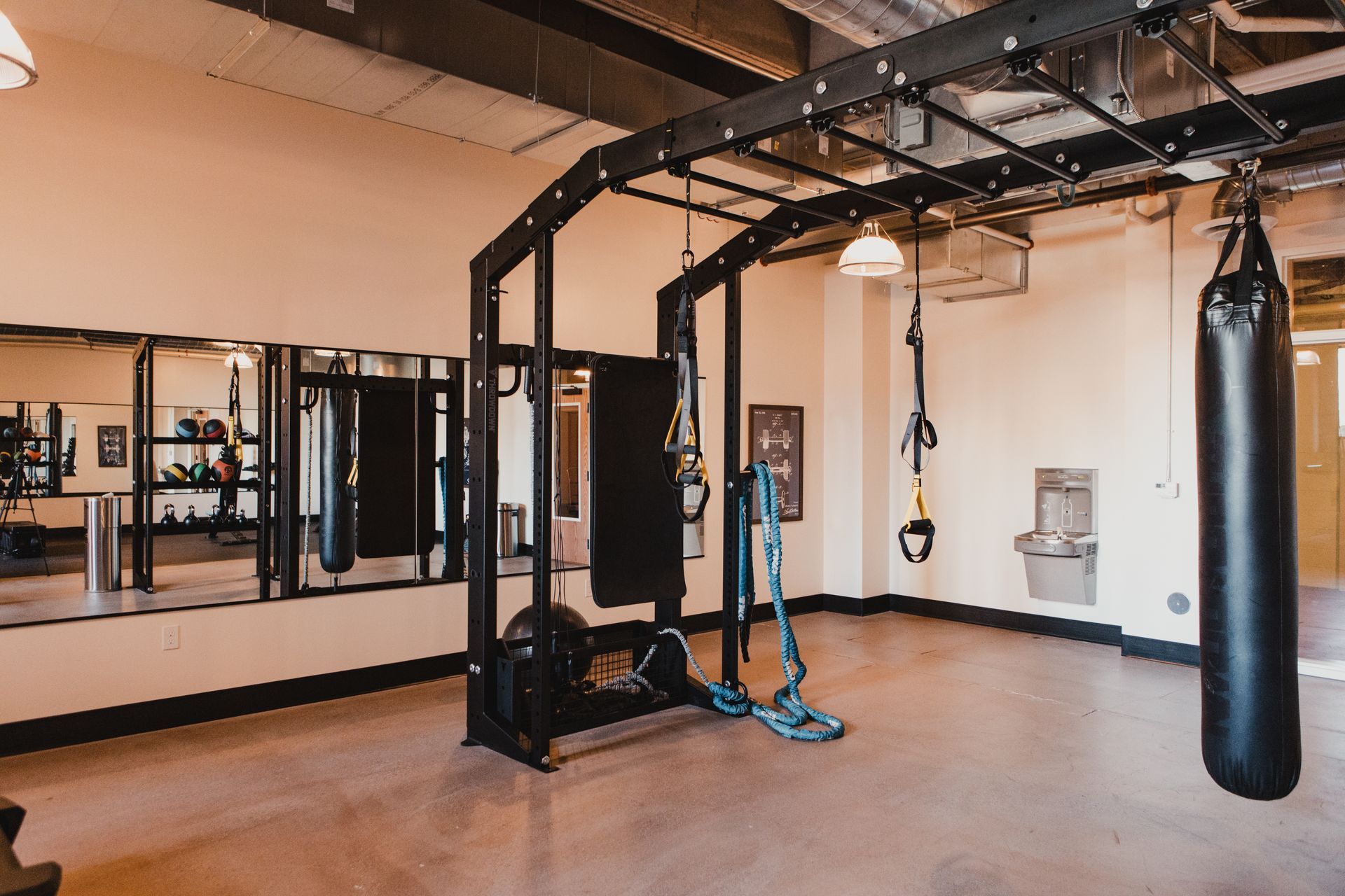Gym with pull-up bars, punching bag, mirrors, and training equipment; light-colored walls and concrete floor.