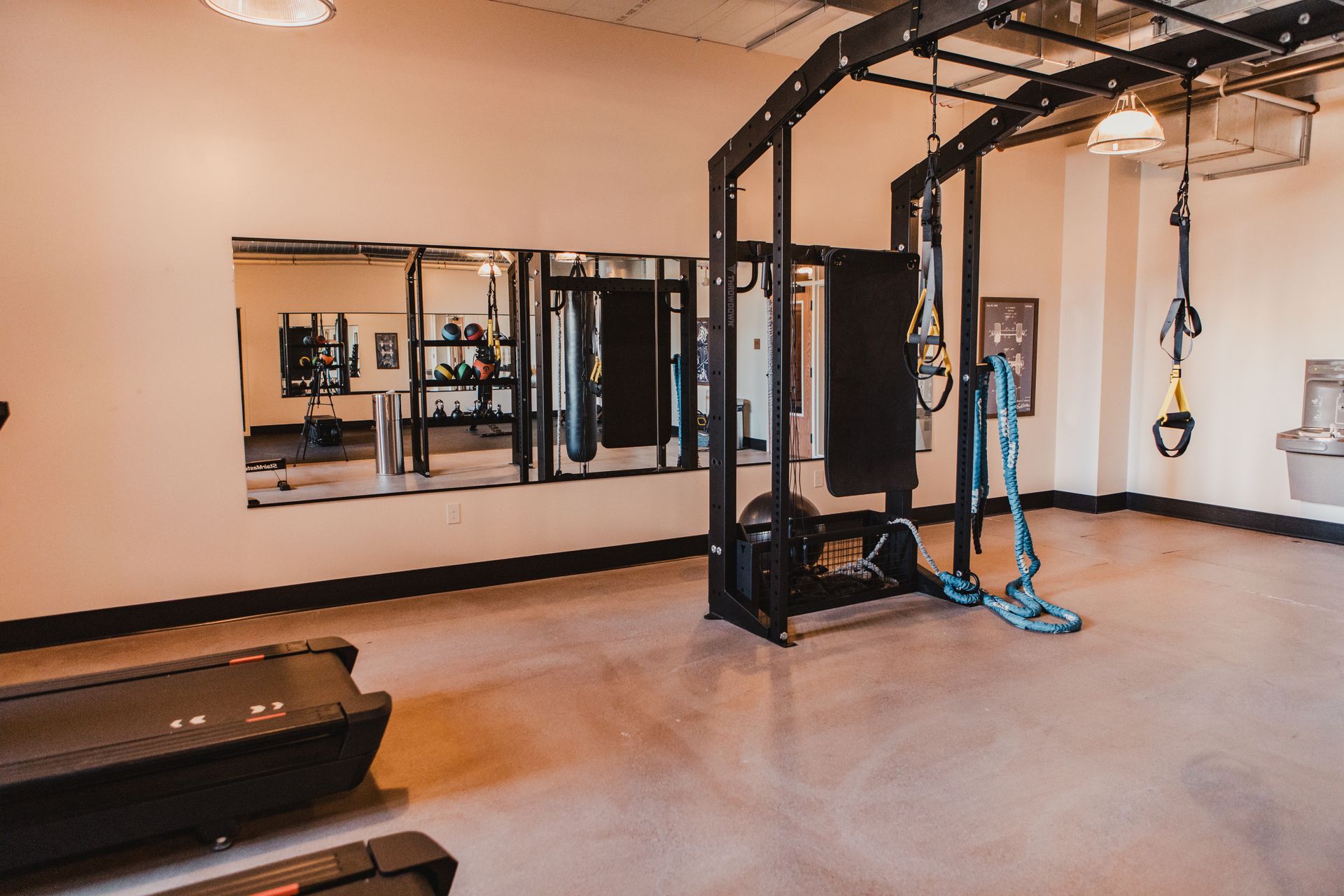 Gym with weight rack, mirrors, treadmill, and exercise equipment. Light brown walls, concrete floor.