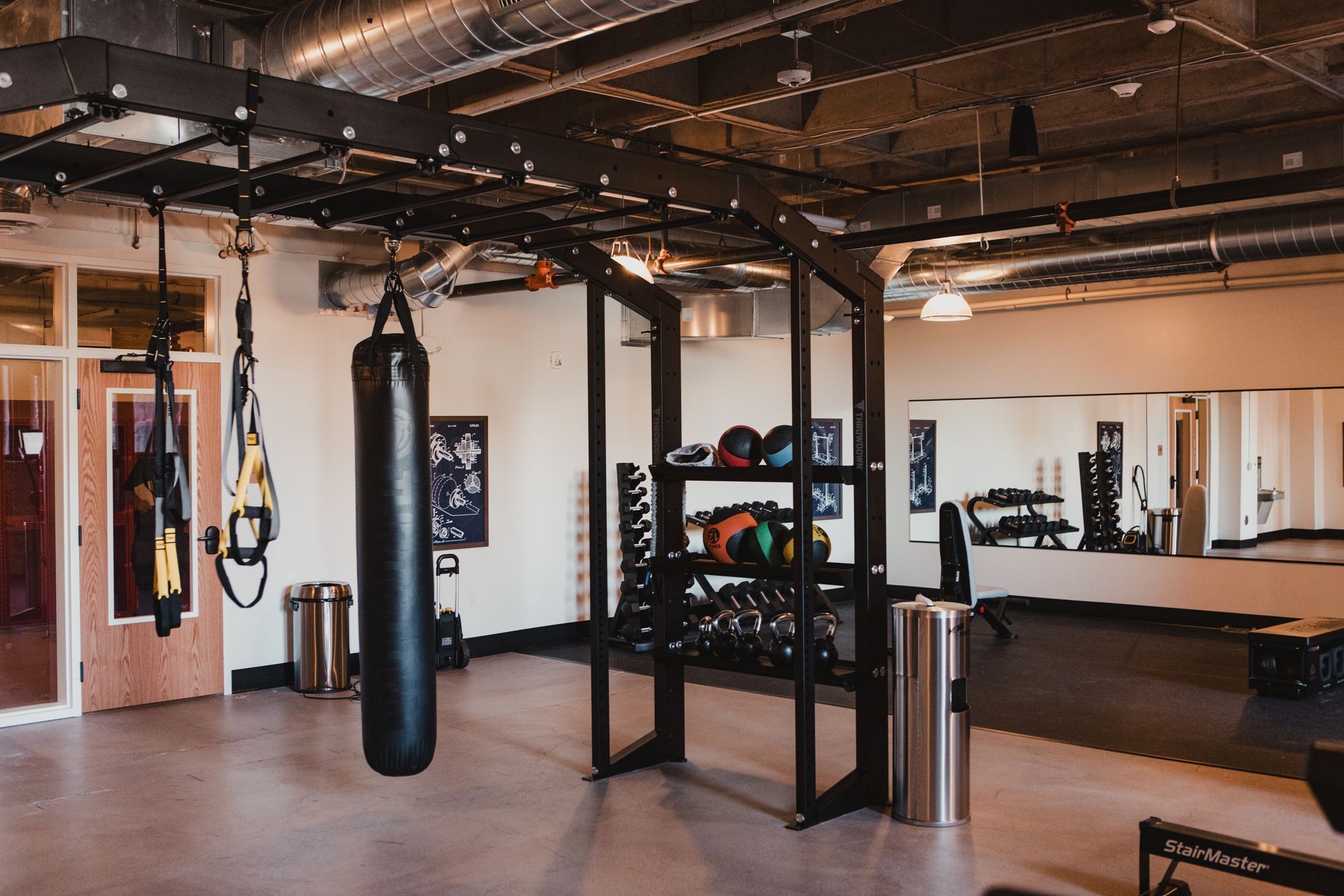 Gym interior with exercise equipment: boxing bag, weights, and TRX straps.