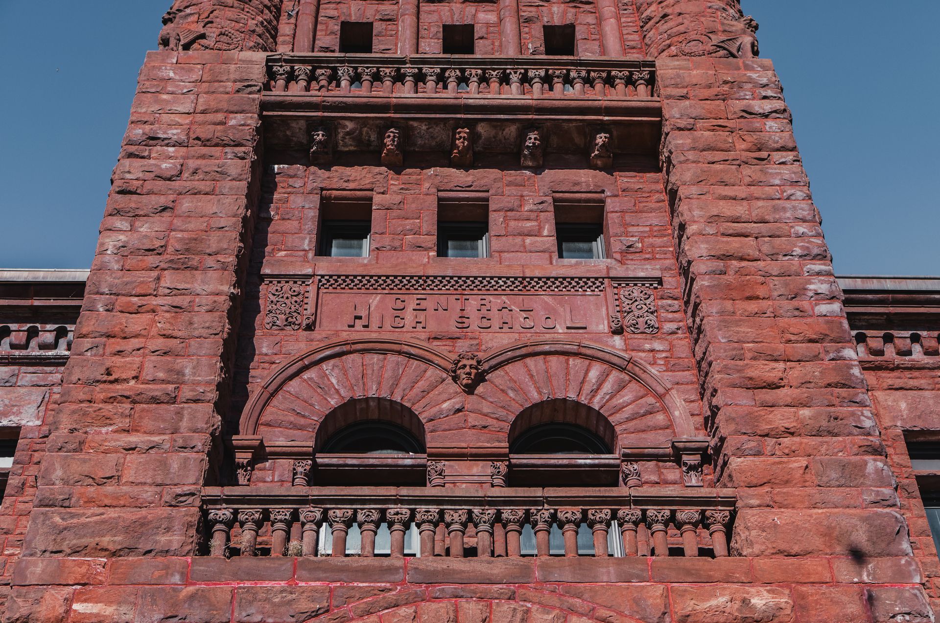 Red brick building facade with arched windows, ornate carvings, and name inscription.