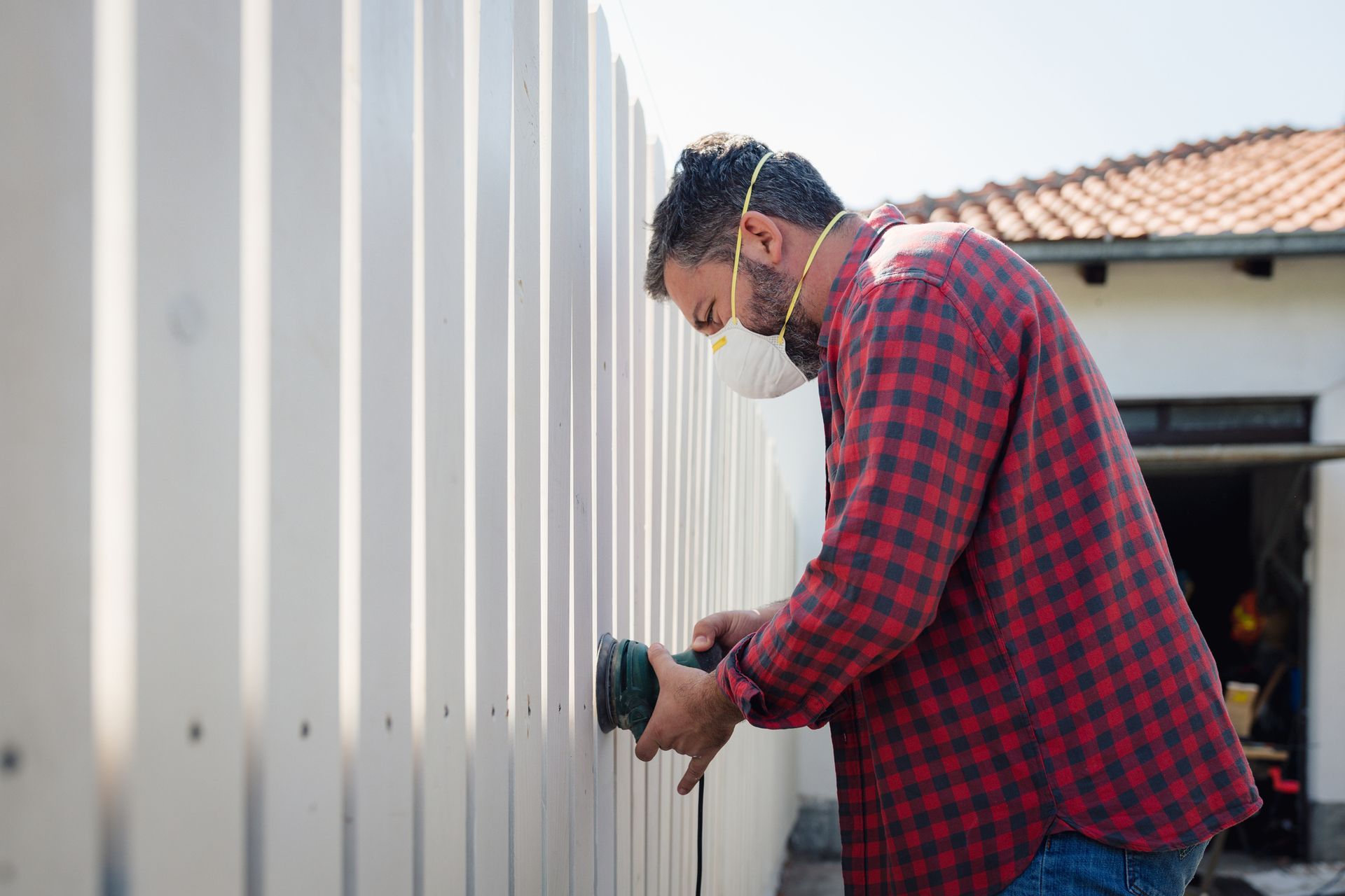 A man uses an electric sander on fence boards, highlighting a professional new fence installation. A man uses an electric sander on fence boards, highlighting a professional new fence installation.