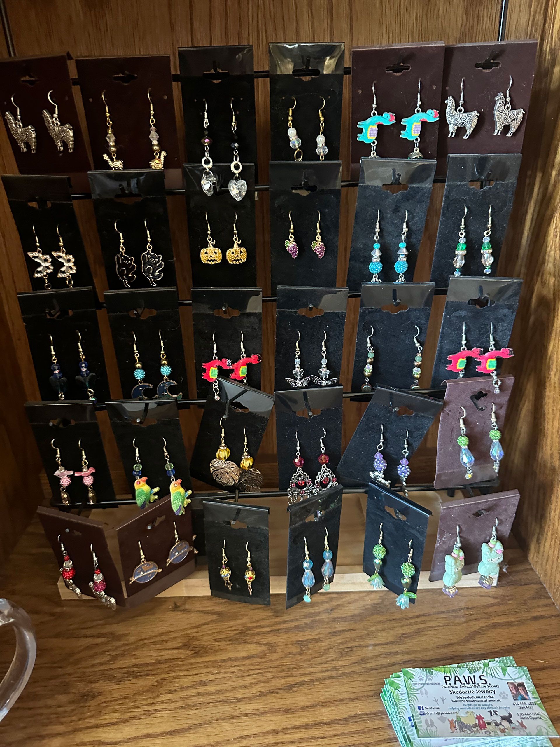 Earrings displayed on black cards in a wooden shelf. Variety of colors and designs.