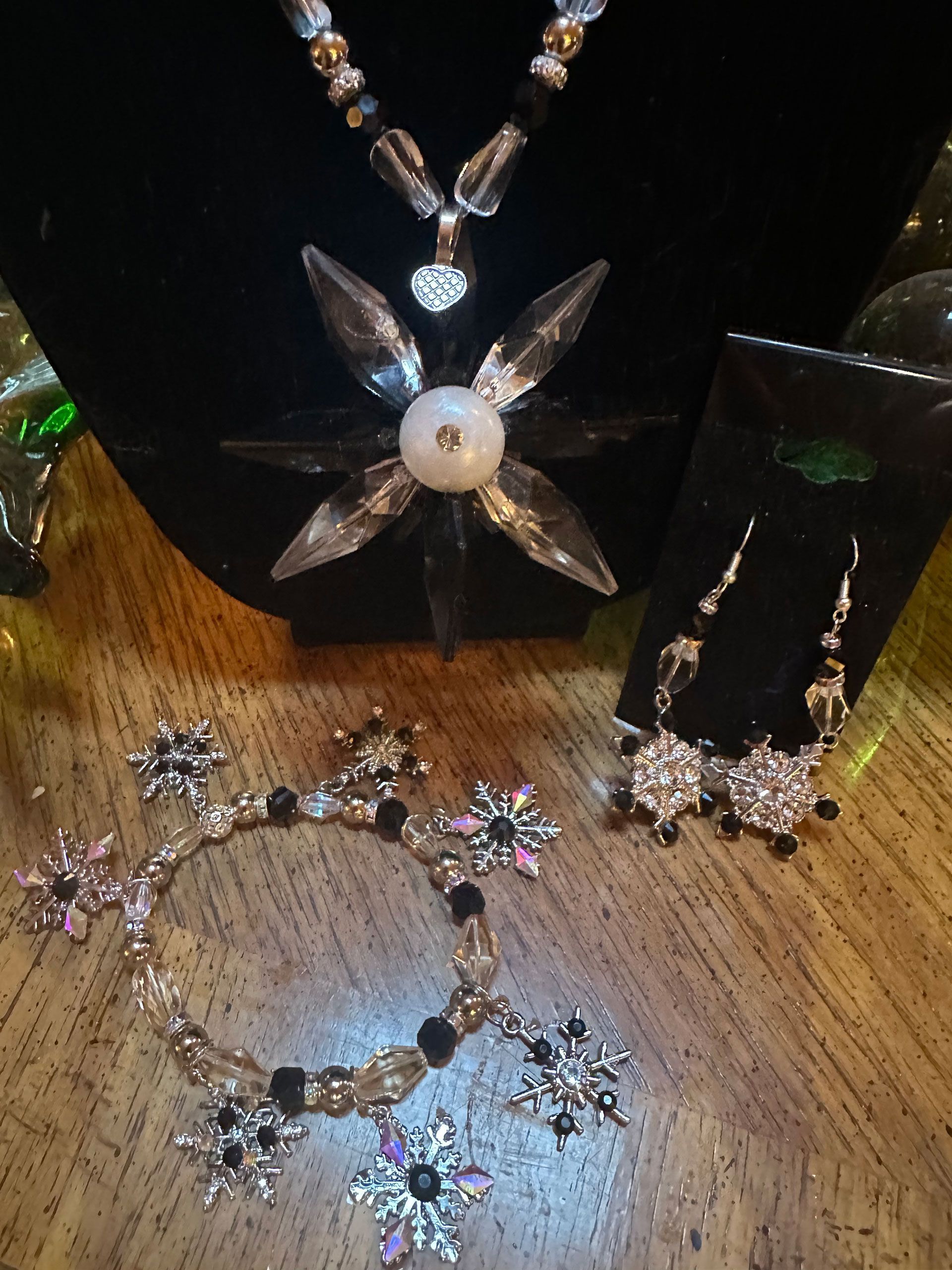 Jewelry set: necklace, earrings, and bracelet with starburst and beaded details, on a wooden surface.