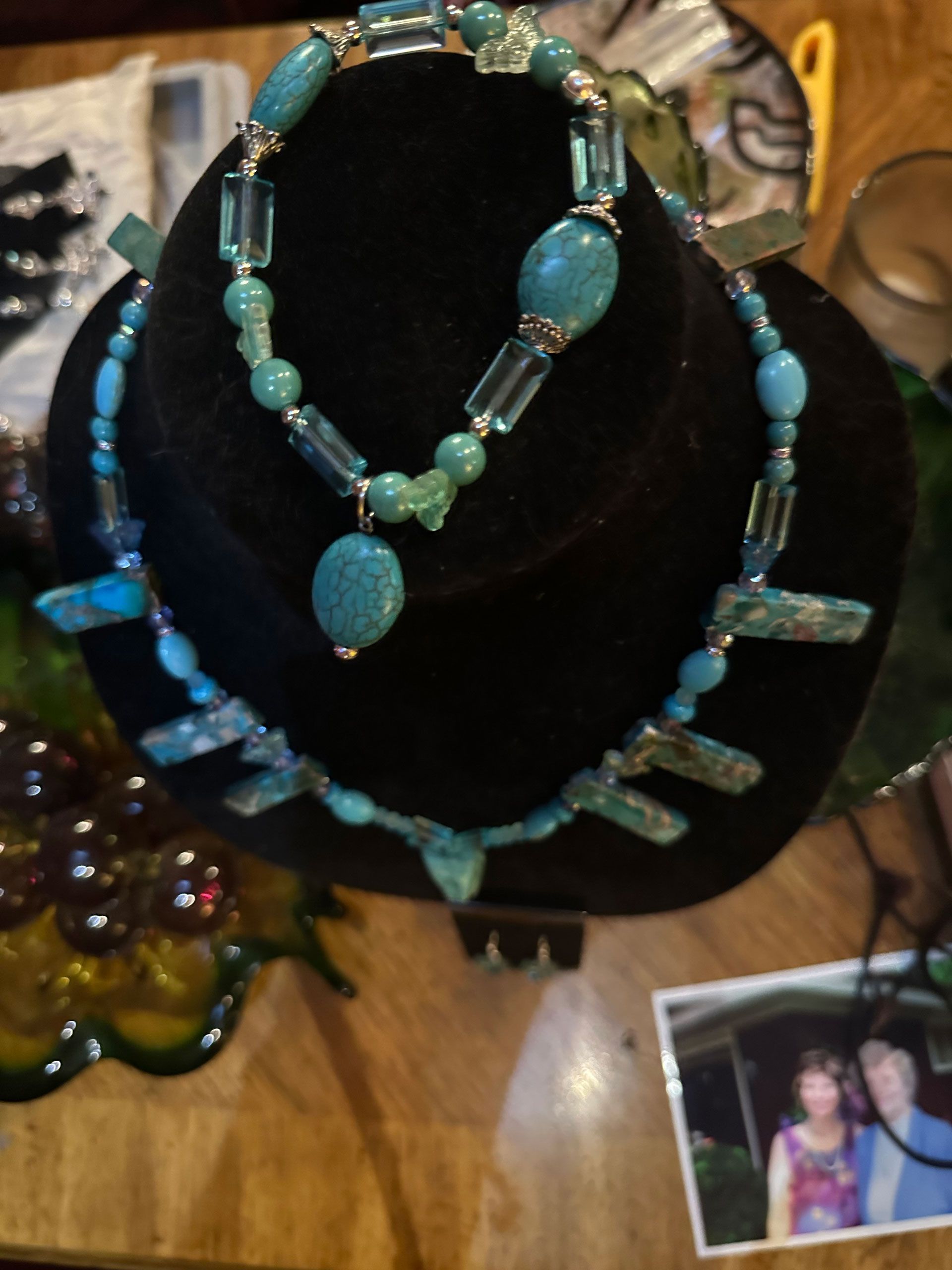 Turquoise beaded necklace and bracelet set on a black display stand. Photo of a couple in the corner.