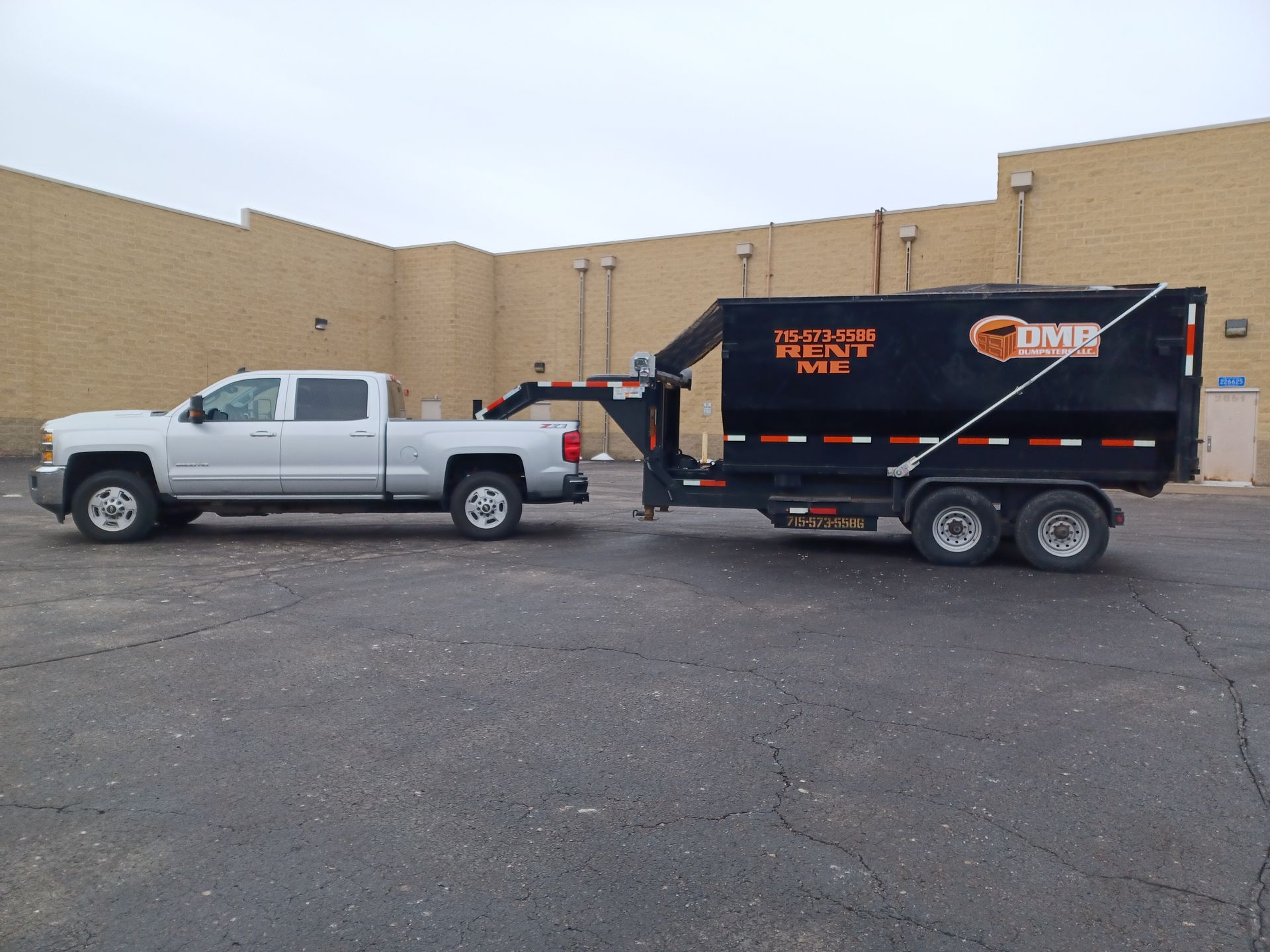 A dumpster is being pulled by a truck in a parking lot