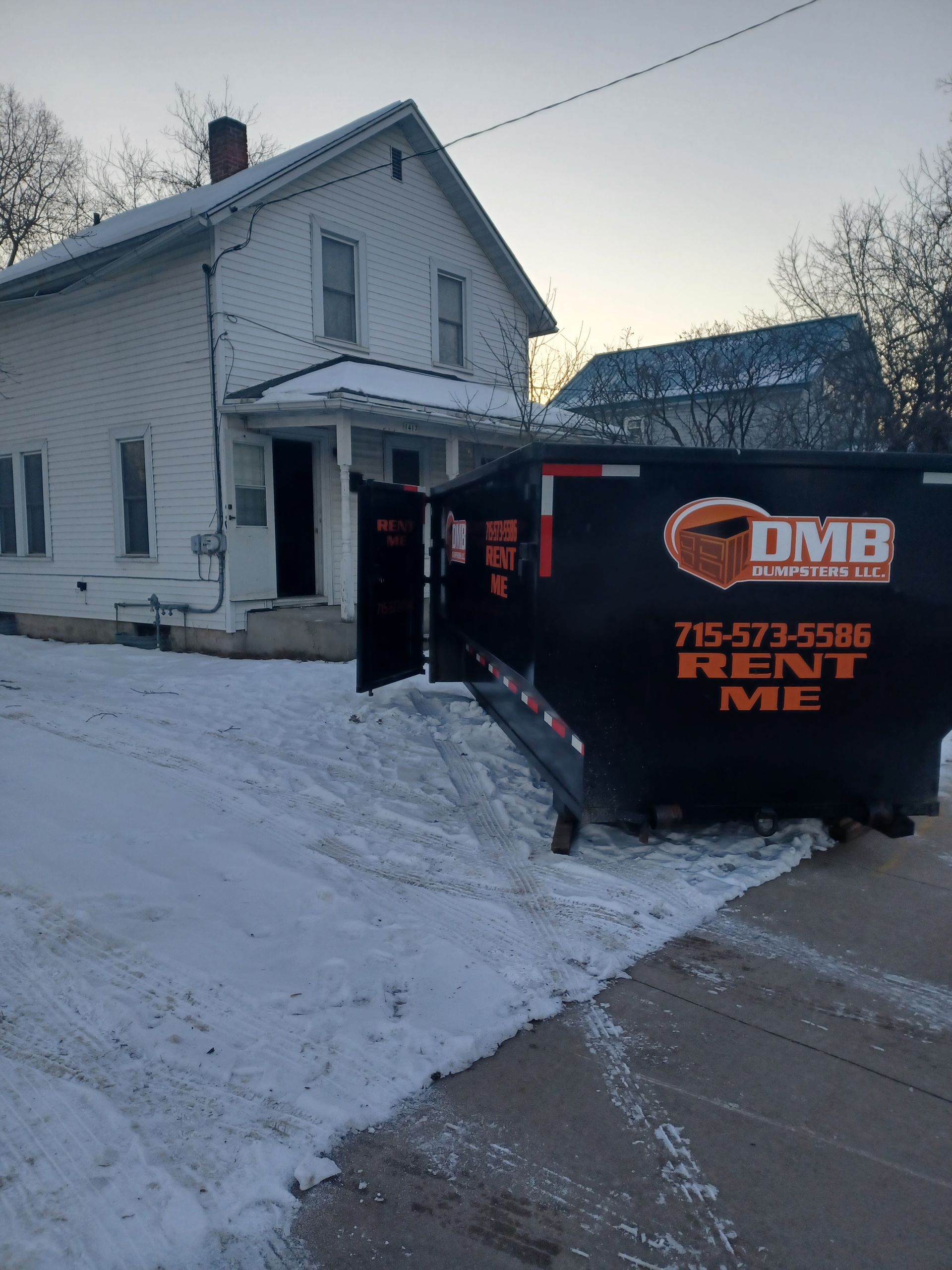 A dumpster is parked in front of a white house.