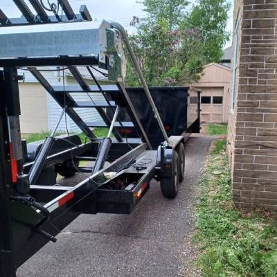 A dumpster trailer is parked in a driveway next to a brick building.