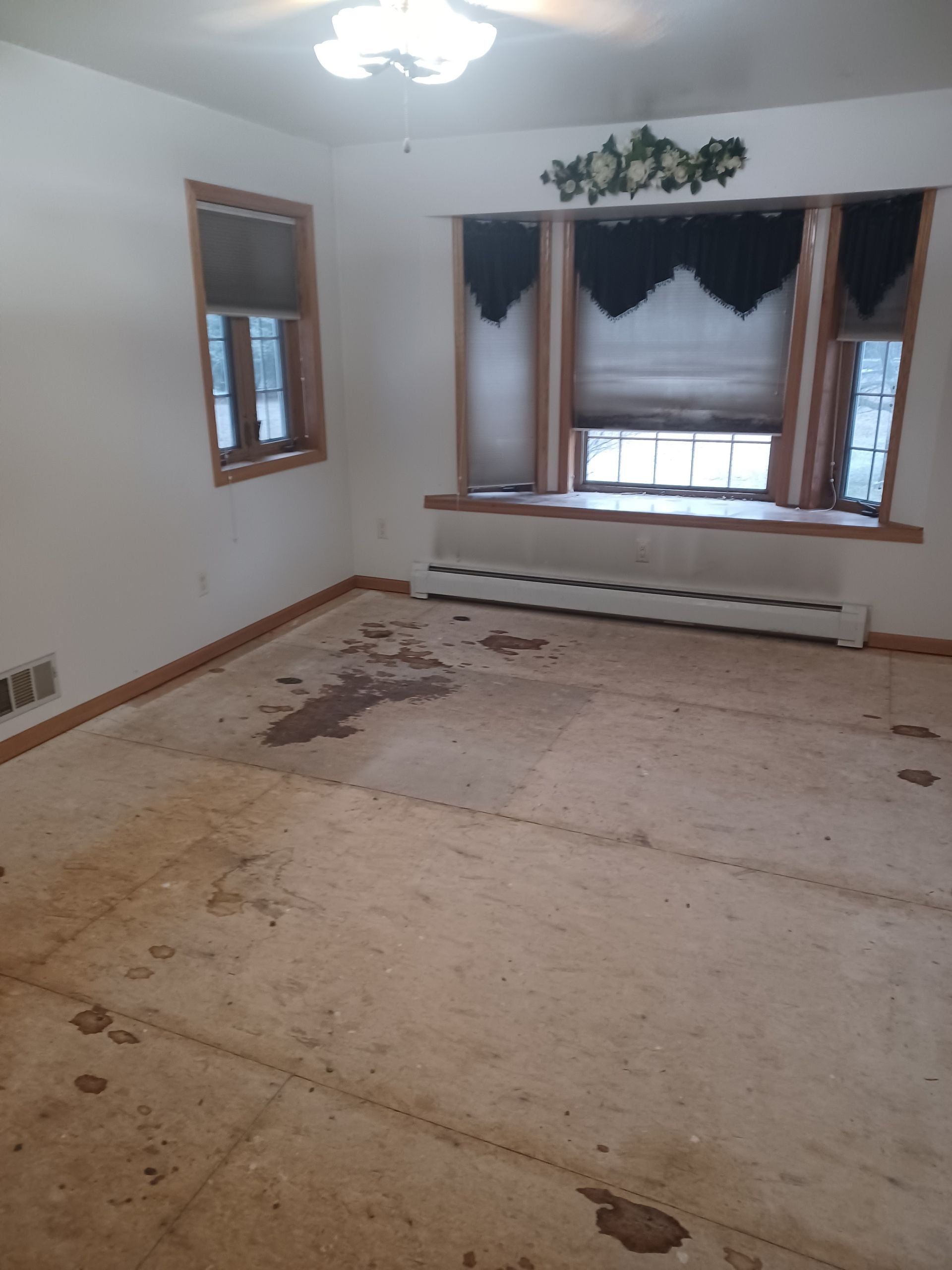 An empty living room with a window and a ceiling fan.