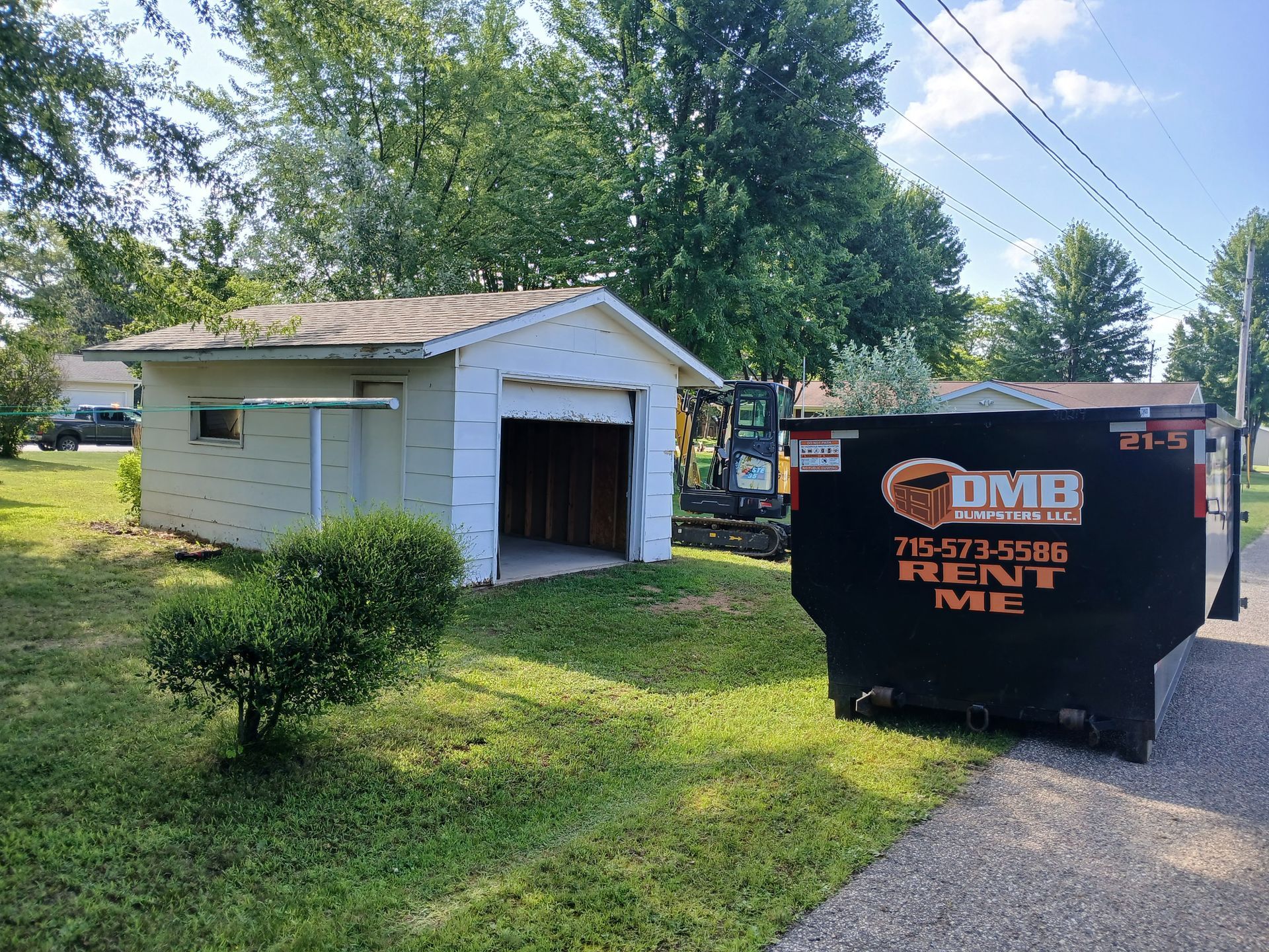 A dumpster is parked in front of a garage.