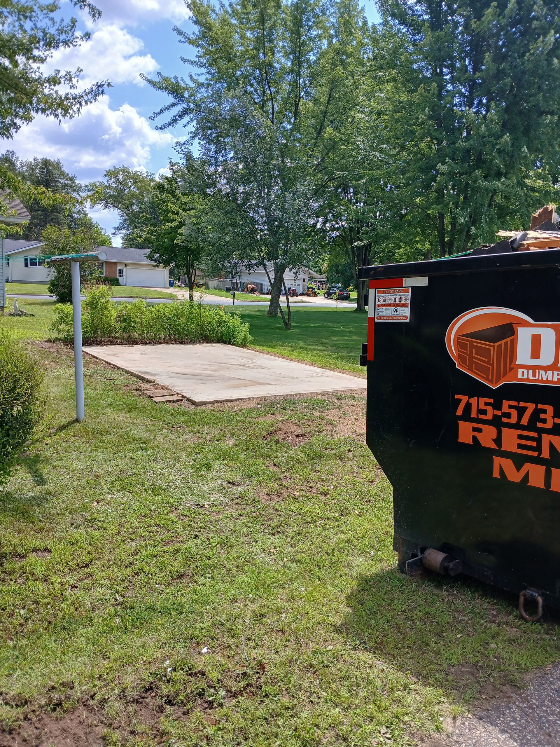 A dumpster is parked in the grass in a yard.