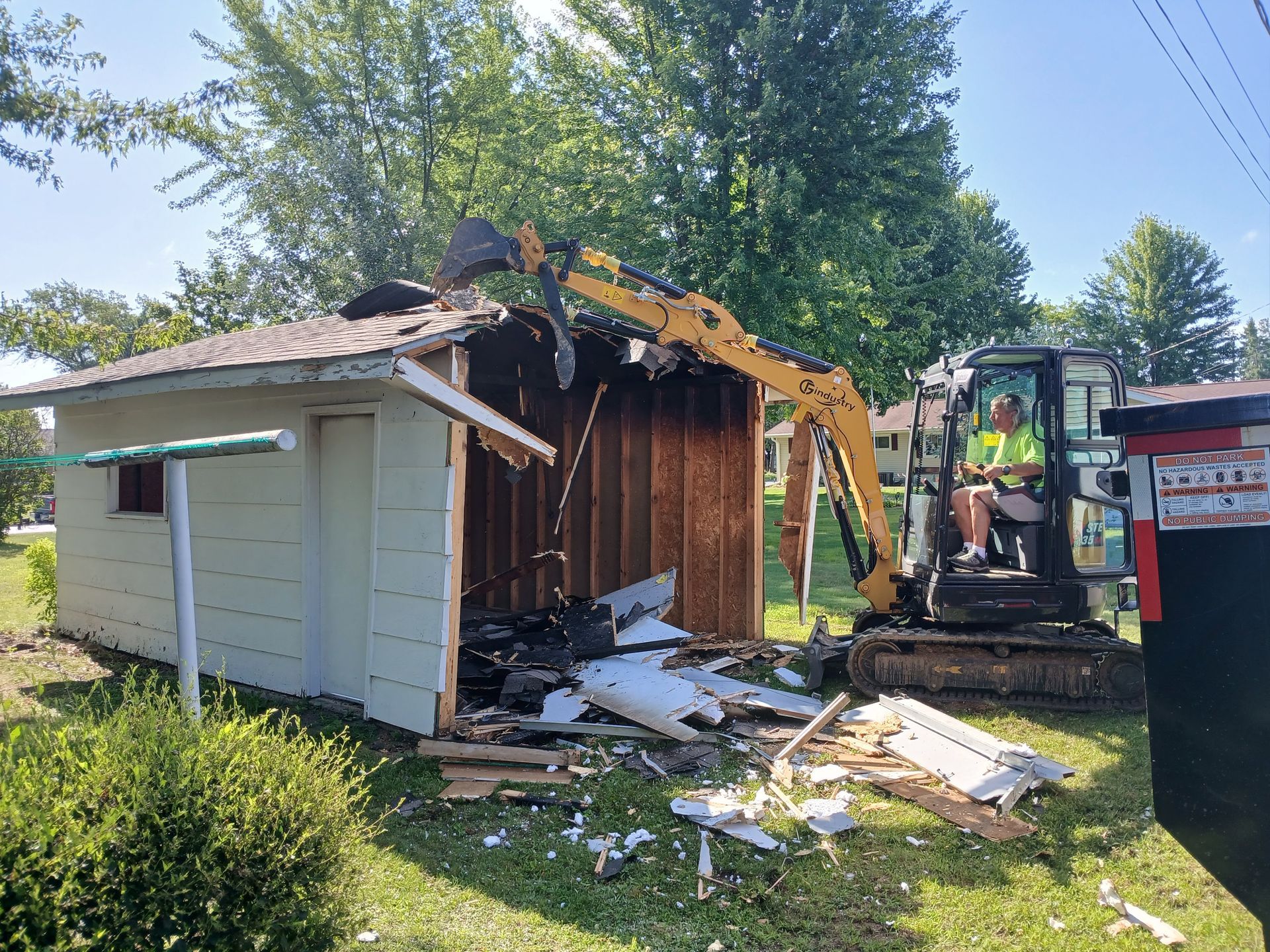 An excavator is demolishing a shed in a yard.