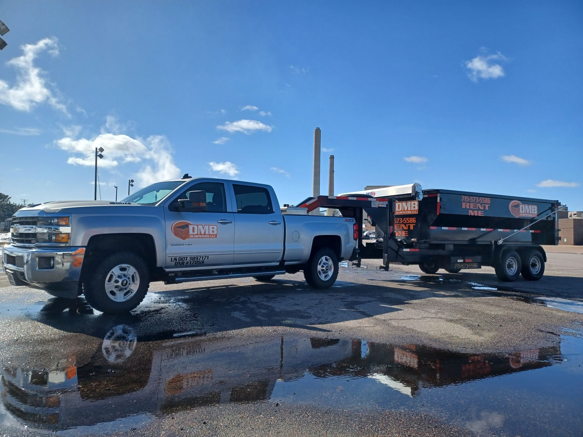 A silver truck is parked next to a dump trailer in a parking lot.