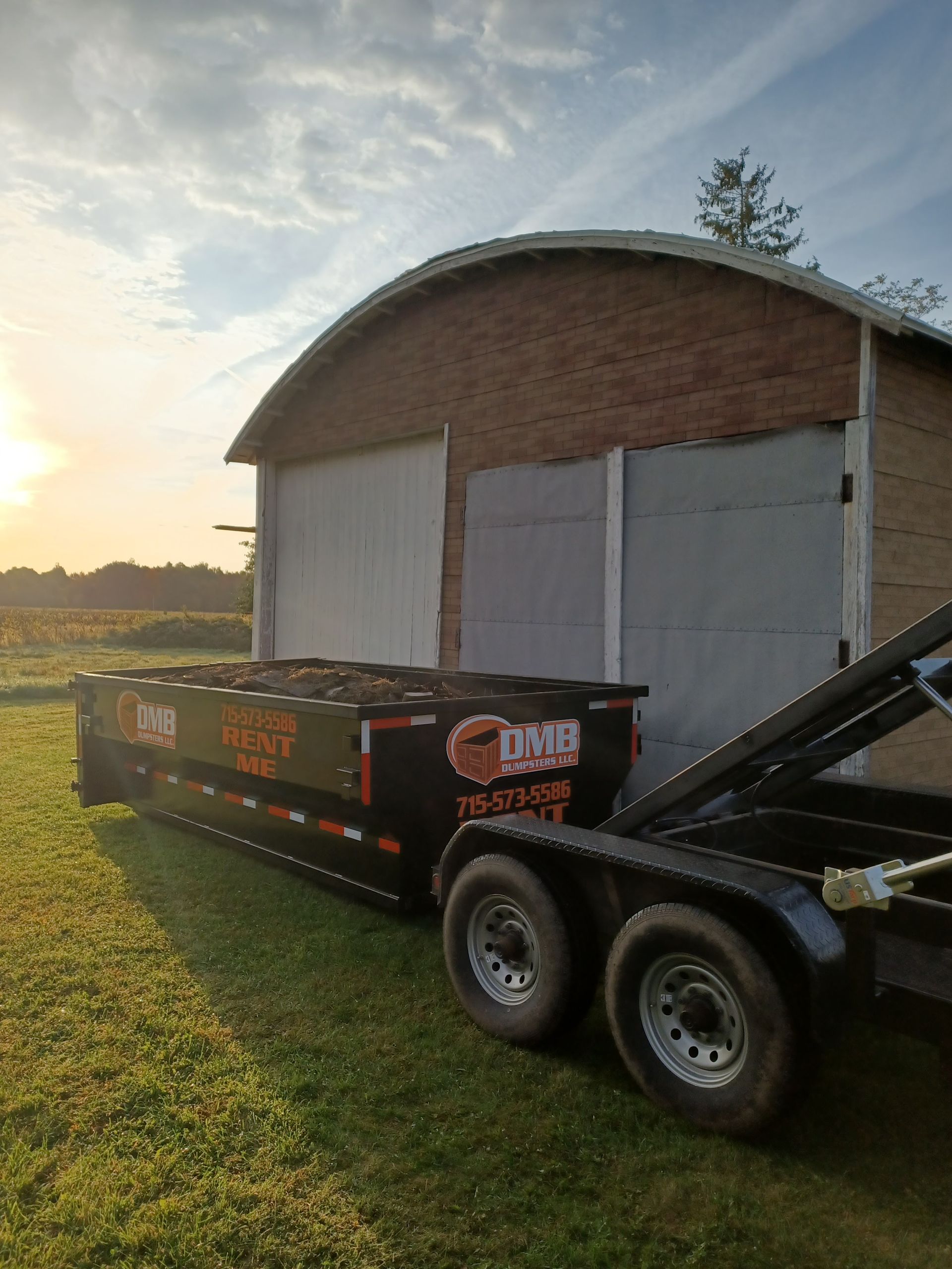 A dumpster on a trailer is parked in front of a brick building.