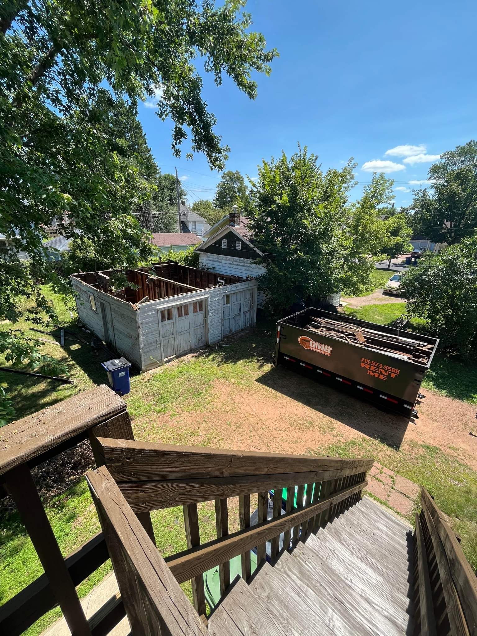 A wooden deck with stairs leading up to a house and a dumpster in the backyard.