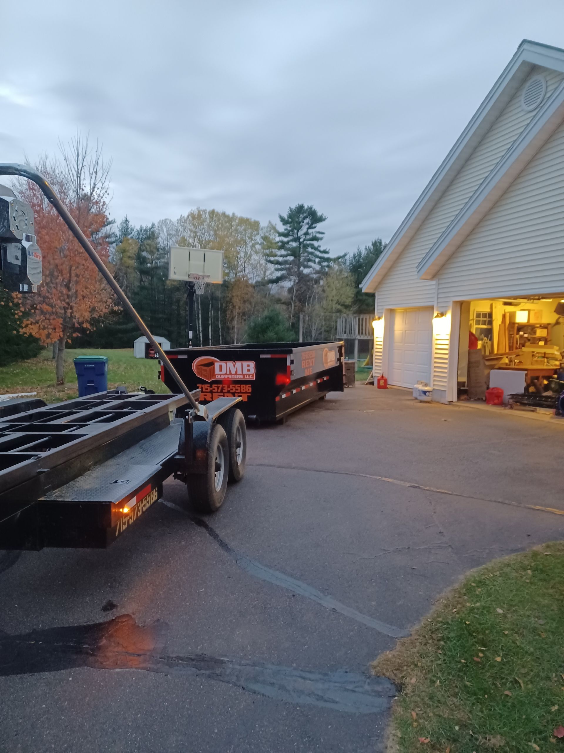 A dump truck is pulling a trailer in front of a garage.