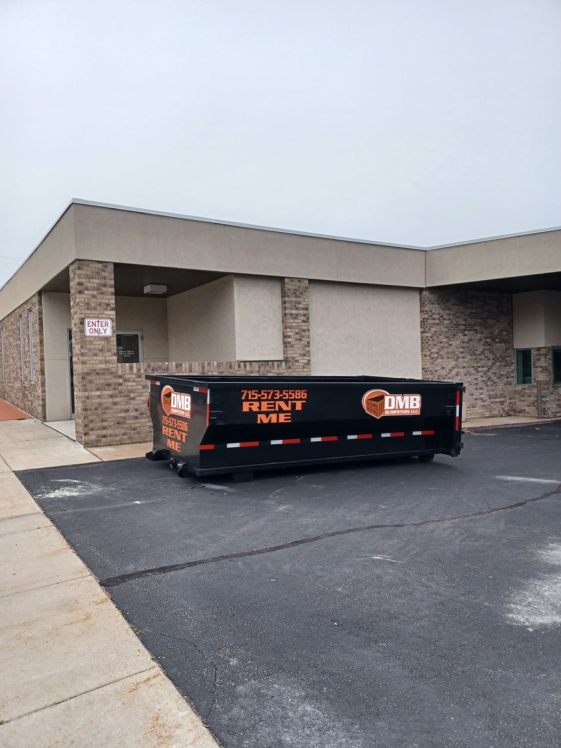 A dumpster is parked in front of a brick building.