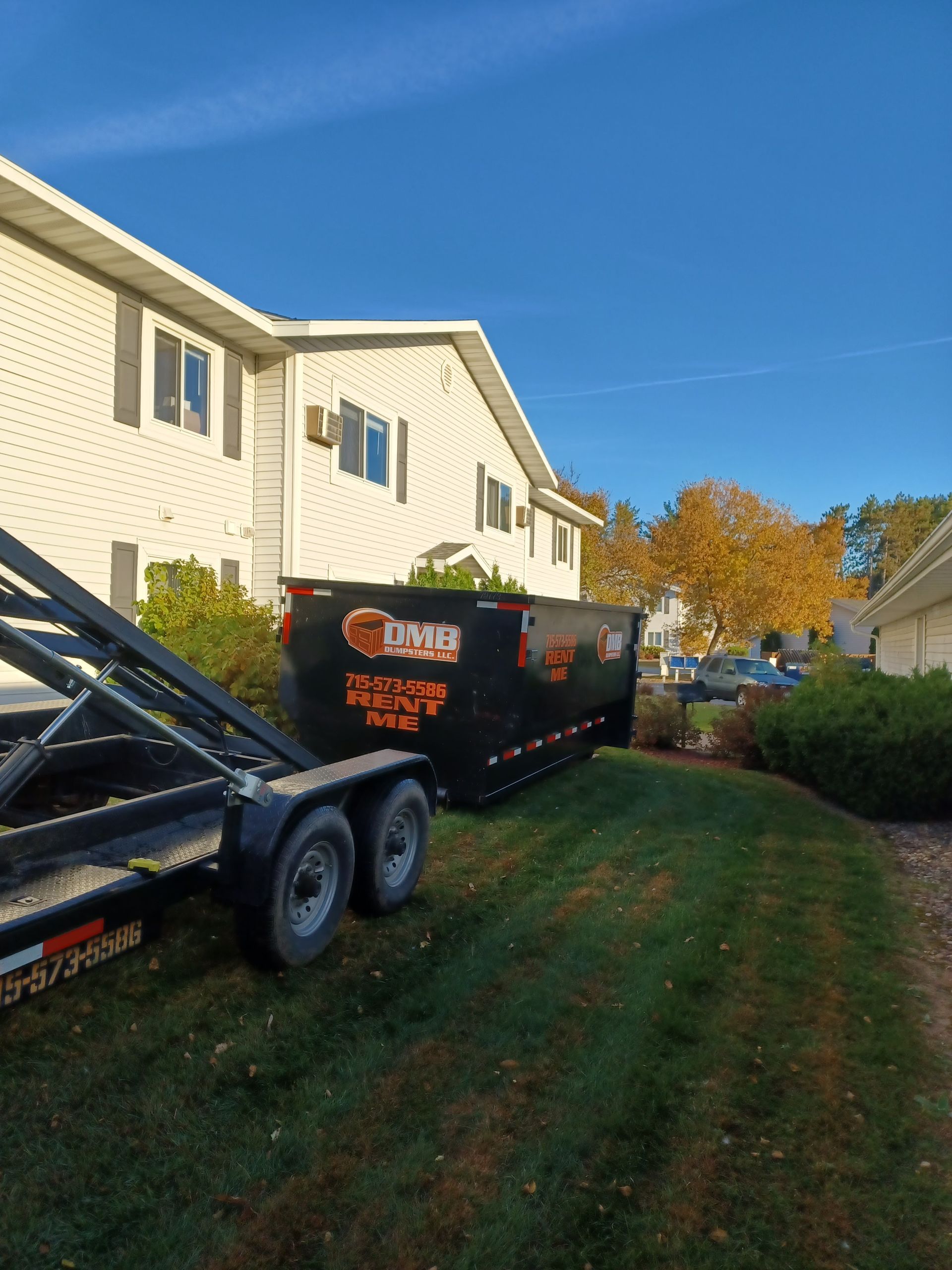 A dumpster on a trailer is parked in front of a house.