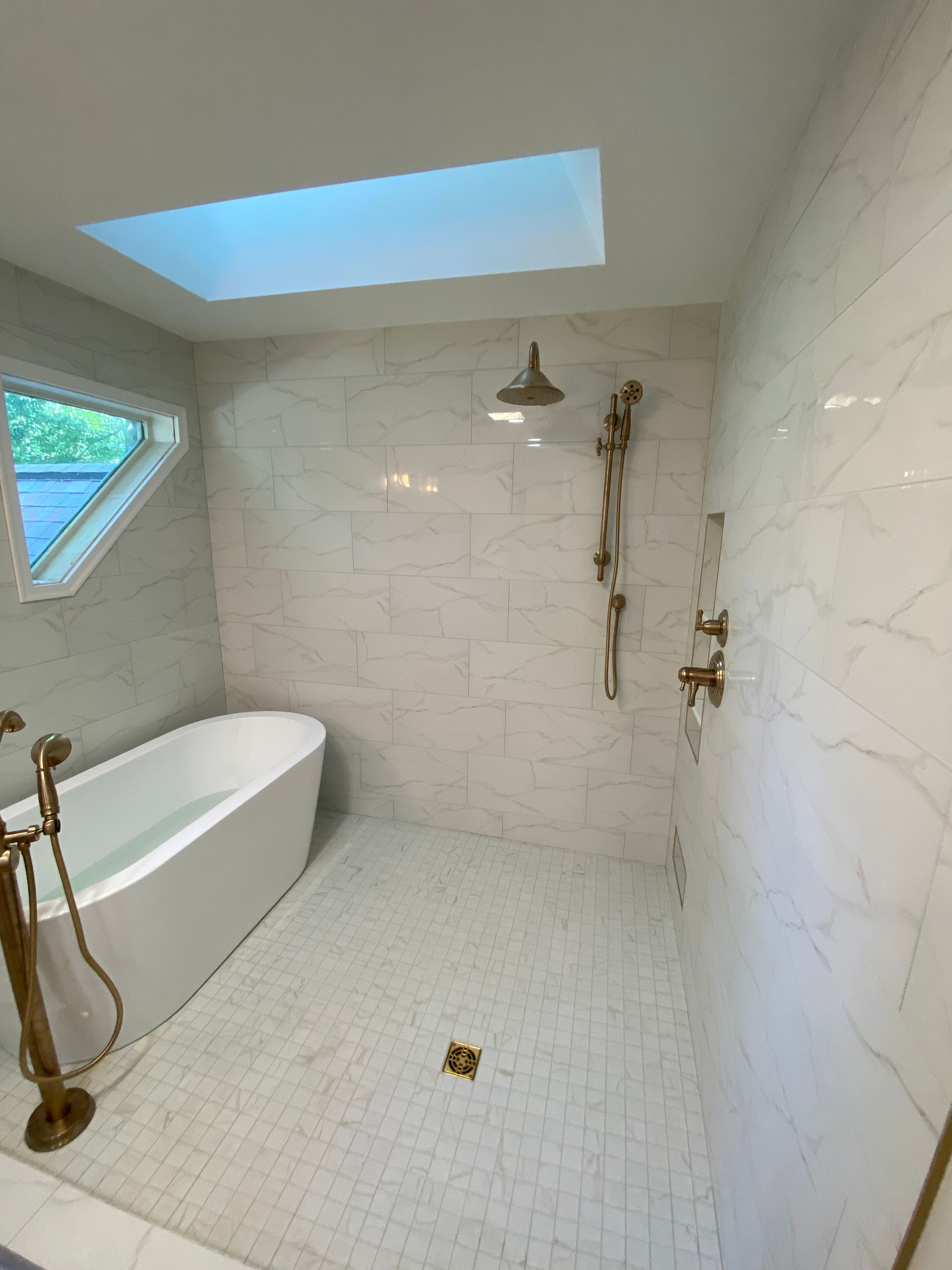 A bathroom with a tub , shower , and skylight.