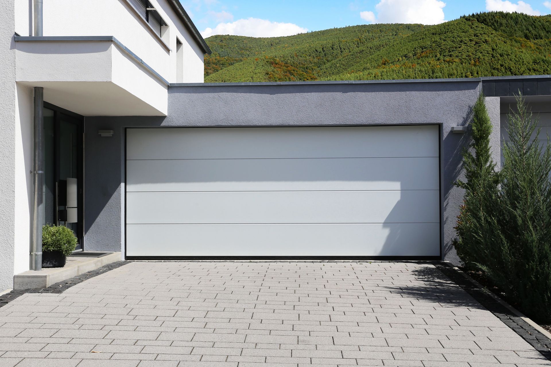 Modern white garage door in a grey house with a paved driveway