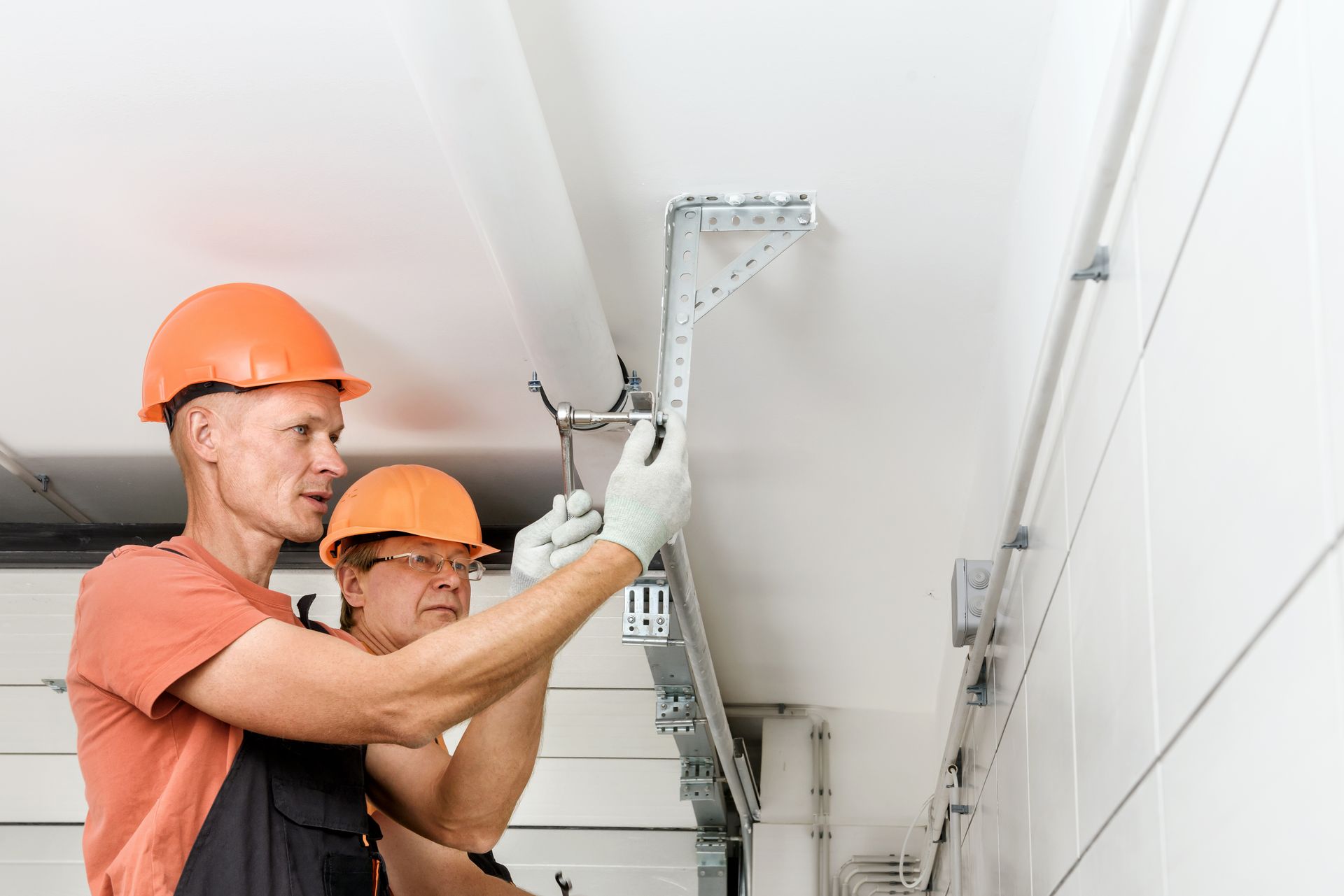 Two workers in hard hats installing a garage door track on a white ceiling