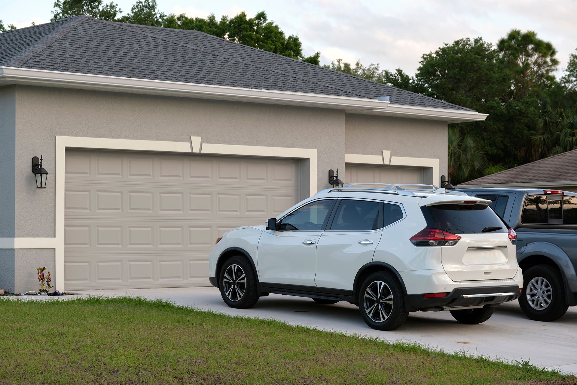 White SUV parked in front of a light gray garage with a dark gray roof