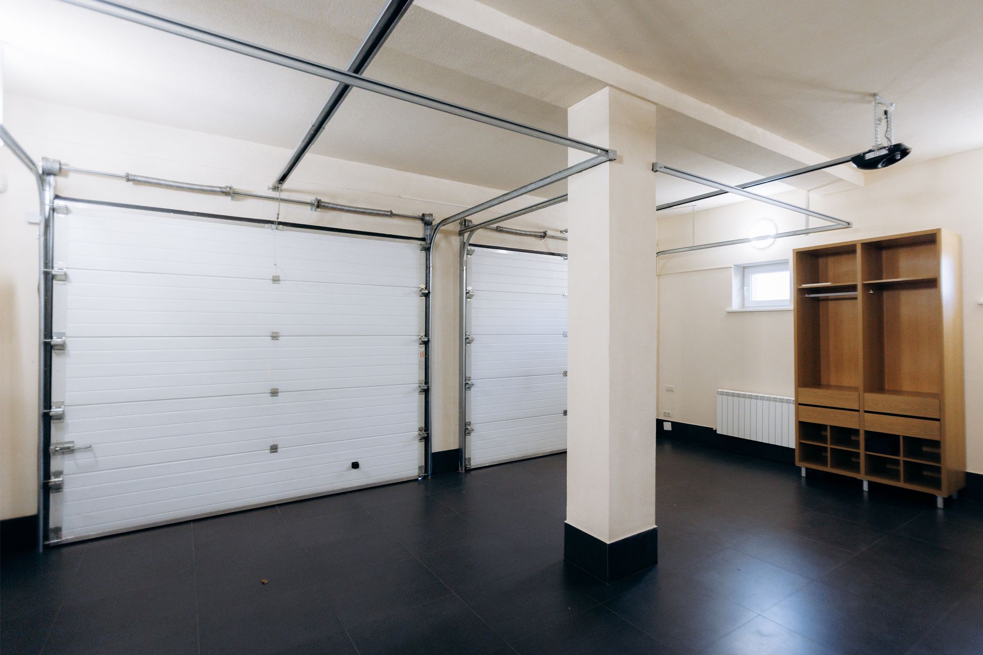 Empty garage with two closed white doors, black floor, beige walls, and wood shelving