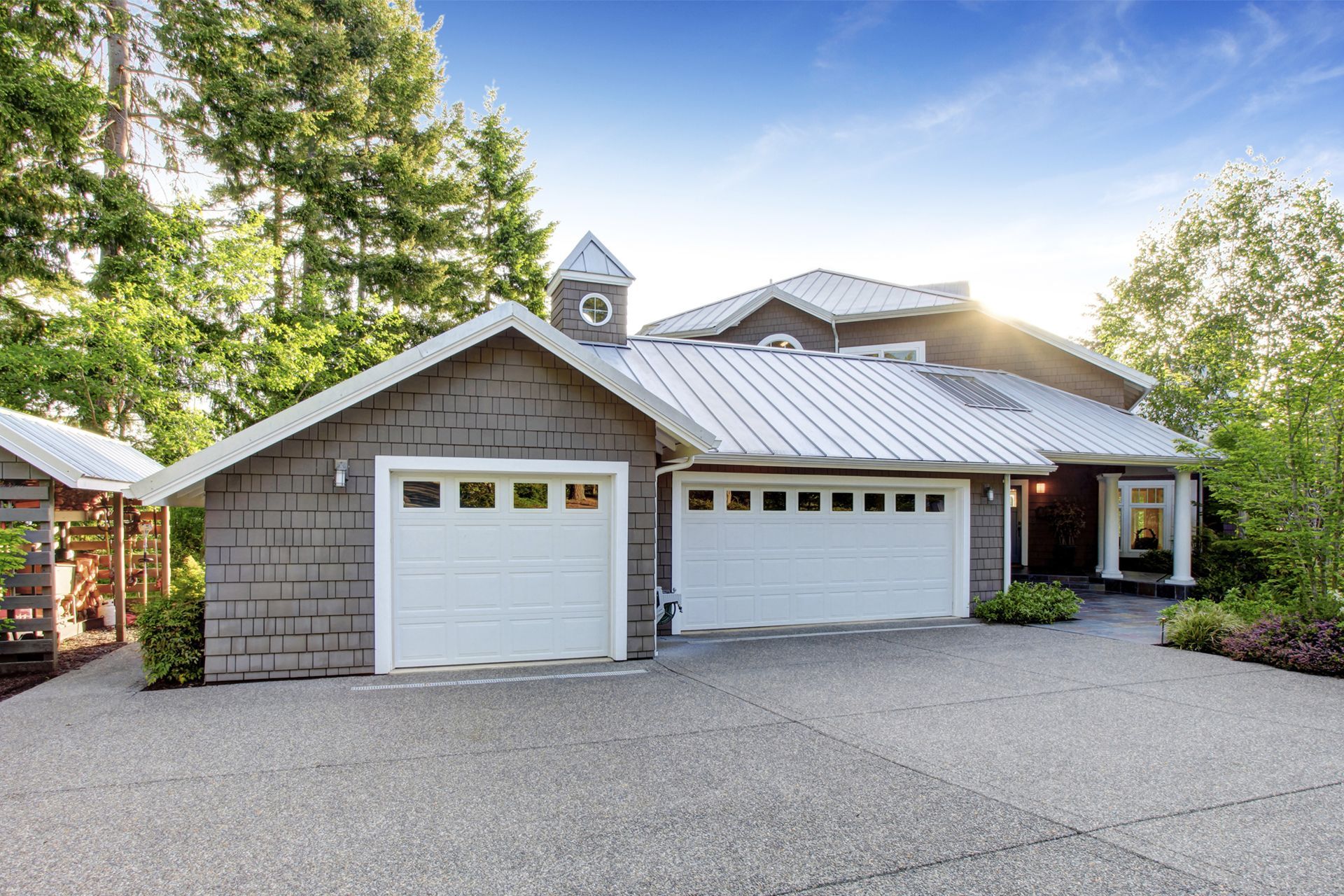 Gray house with white garage doors, asphalt driveway, and green trees