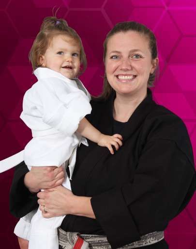 a woman in a karate uniform is holding a little girl in her arms .