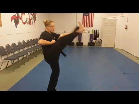 A woman is kicking her leg in a martial arts gym