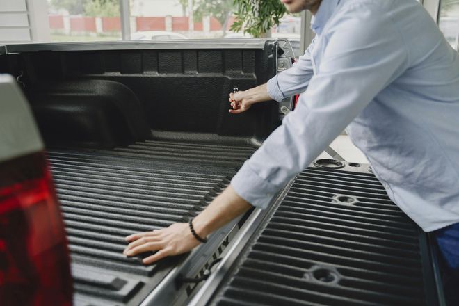 Man in a blue shirt opens the tailgate of a black pickup truck. Man in a blue shirt opens the tailgate of a black pickup truck.
