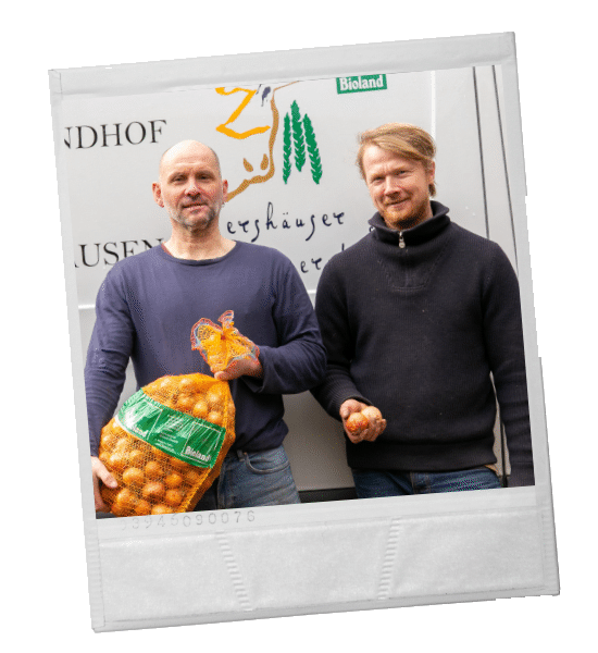 Zwei Männer in einer Scheune mit Flaschen und Eiern, im Hintergrund Kühe.