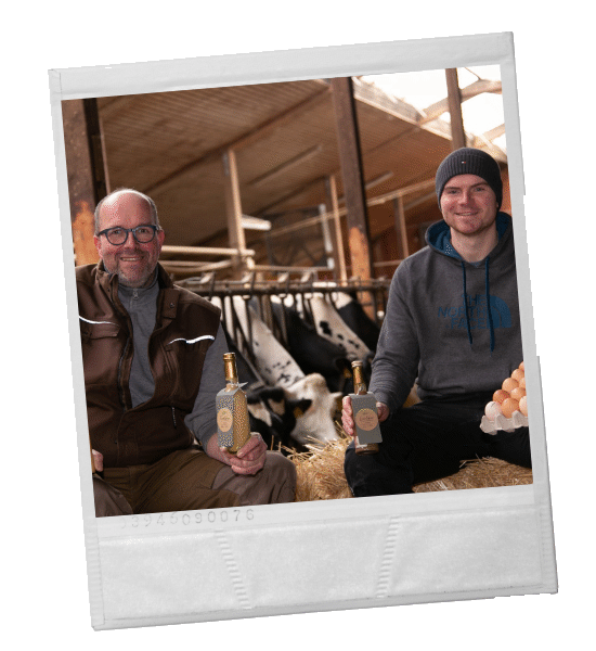 Zwei Männer in einer Scheune mit Flaschen und Eiern, im Hintergrund Kühe.