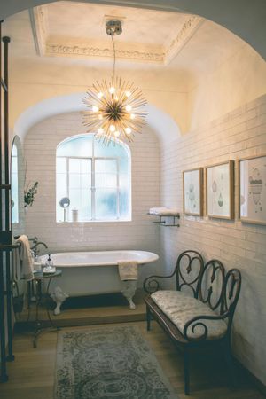 A bathroom with a tub , bench and chandelier.