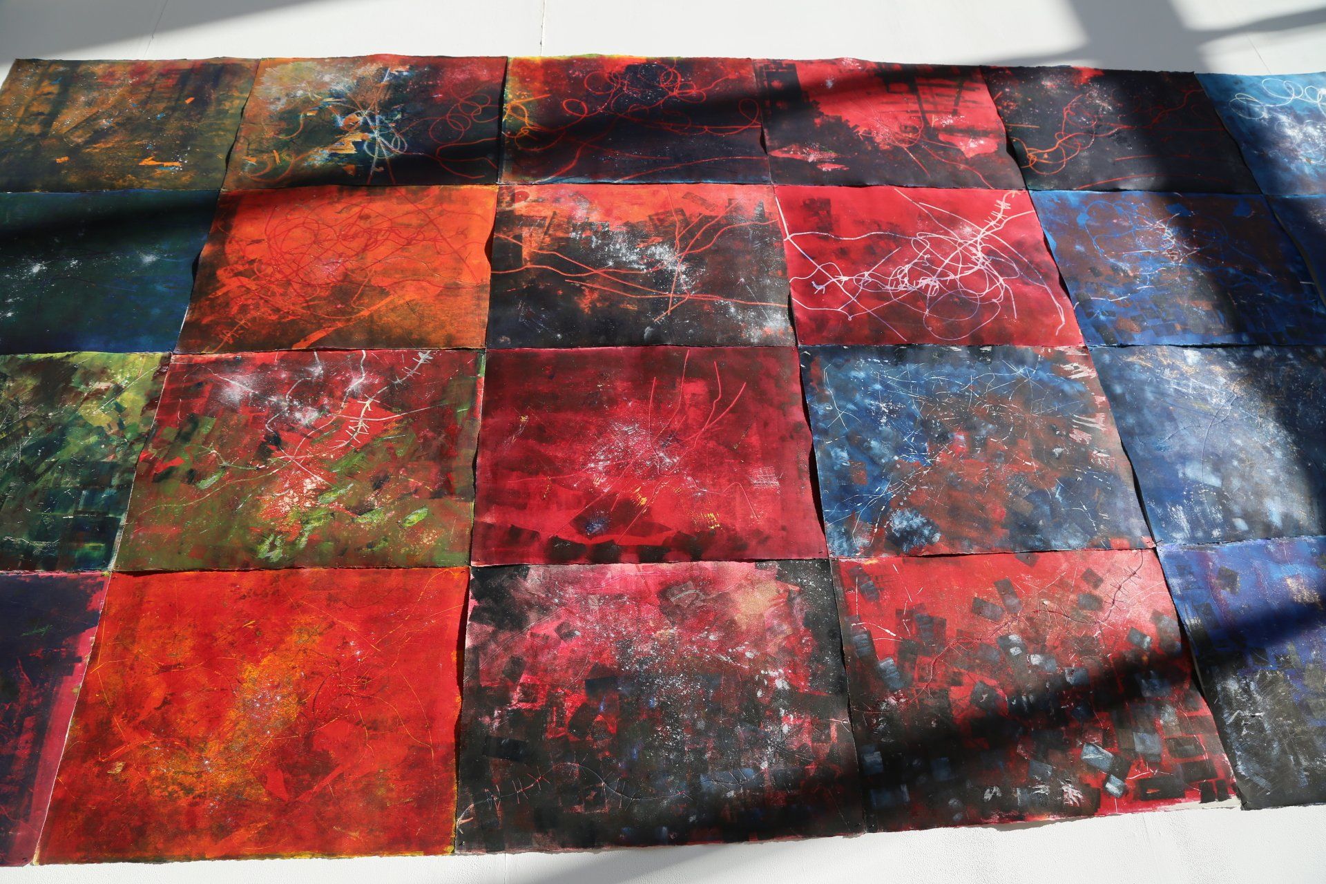 Abstract artwork: square panels of vibrant, mottled colors. Reds, blues, oranges, and blacks are arranged in a grid.