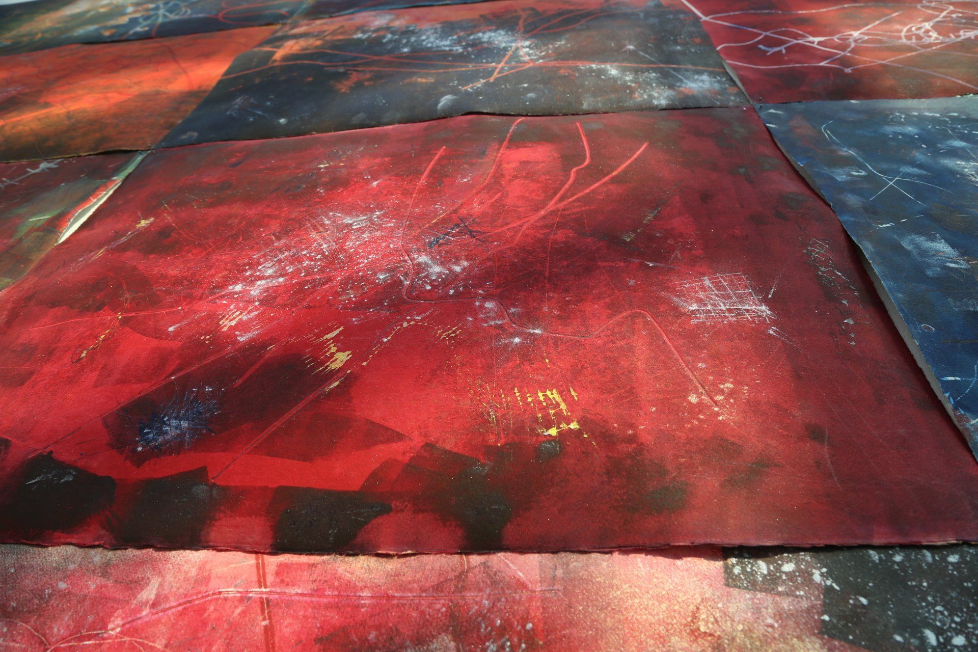 Abstract artwork of red, black, and blue squares. Splatters and brushstrokes create textured patterns.